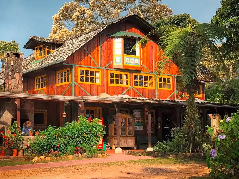 Farbenfrohe Sachatamia-Lodge mit roter Holzfassade und gelben Fenstern im Nebelwald von Mindo, umgeben von tropischen Pflanzen.