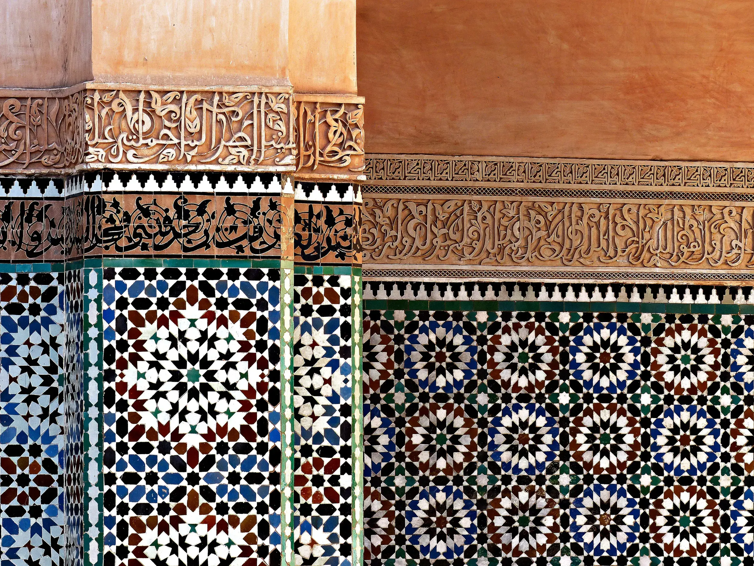 Nahaufnahme kunstvoller, bunter Mosaike und Stuckverzierungen mit Kalligrafie an der Wand der Medersa Ben Youssef in Marrakesch.