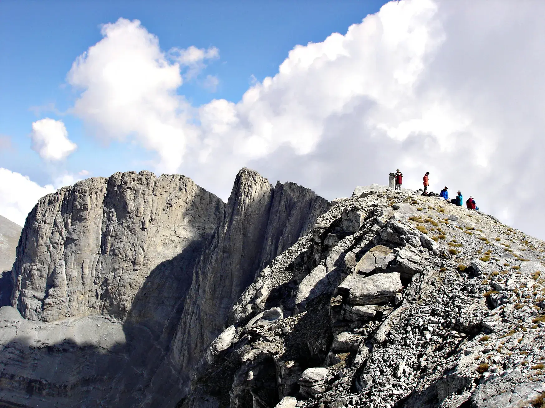 Eine Wandergruppe erreicht den felsigen Gipfel des Skolio im Olymp-Massiv und genießt die Aussicht auf die Bergwelt Griechenlands.