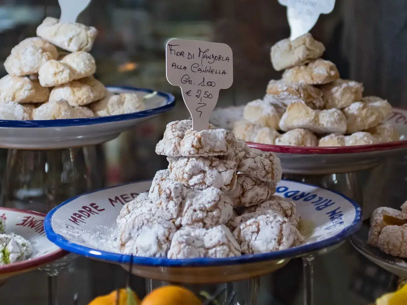 Mit Puderzucker bestäubtes Mandelgebäck, Fior di Mandorla, aufgetürmt auf Keramiktellern in der Auslage einer Pasticceria.