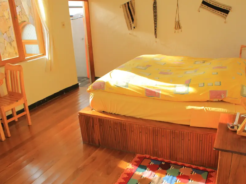 Sonnendurchflutetes Zimmer in der Ecolodge La Estancia am Titicacasee mit Holzbett und traditioneller Aymara-Dekoration.