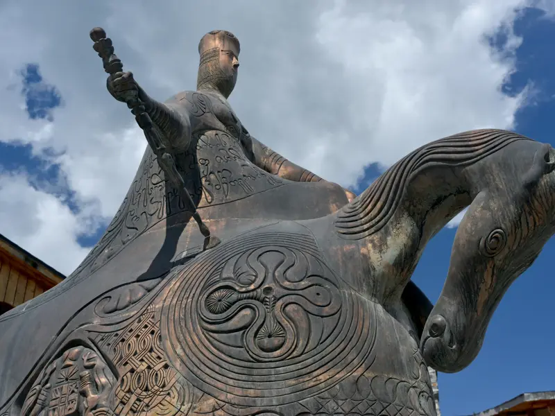 Imposante Reiterstatue von Königin Tamar in Mestia, Swanetien, mit detaillierten, kunstvollen Gravuren vor bewölktem Himmel.