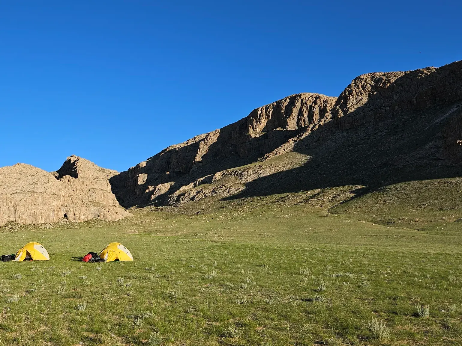 Zwei gelbe Trekking-Zelte in der weiten, grünen Steppe am Fuße des felsigen Bergmassivs Ikh Khairkhan in der Mongolei.