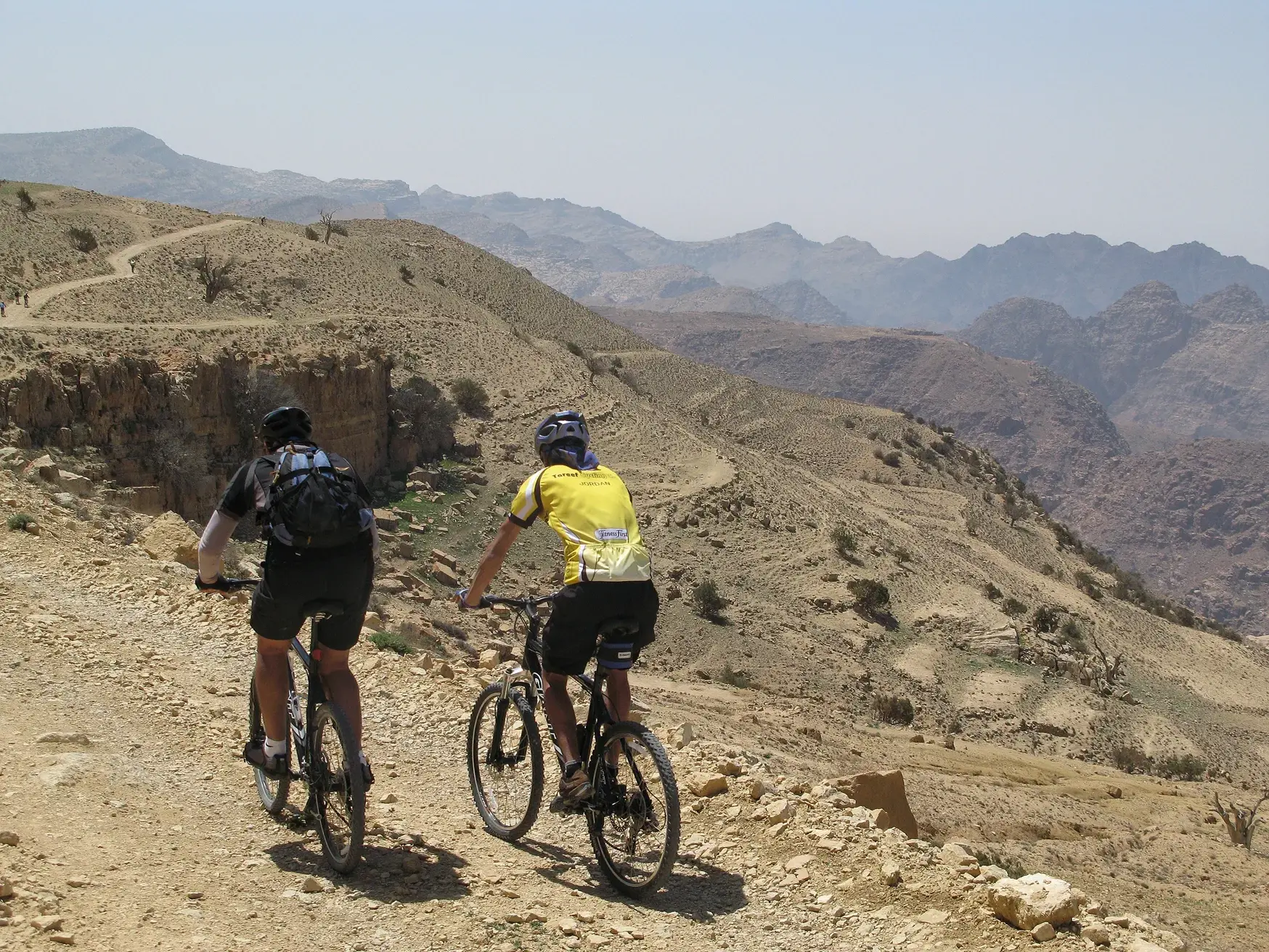 Zwei Mountainbiker auf einer geführten Radreise erkunden einen Offroad-Pfad in der weiten, kargen Bergwelt Jordaniens.