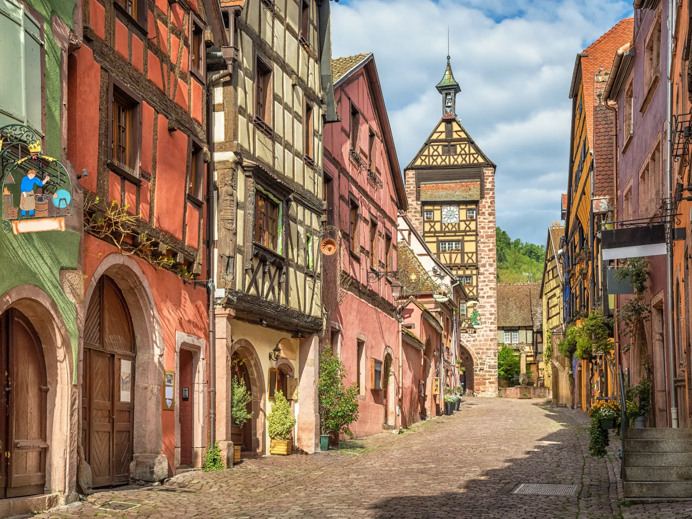 Eine malerische Gasse mit Kopfsteinpflaster und bunten Fachwerkhäusern in Riquewihr an der Elsässer Weinstraße.