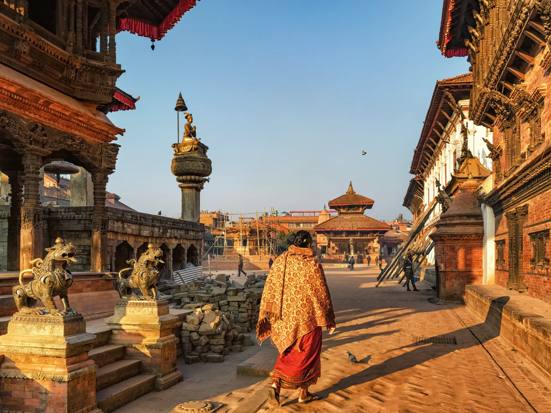 Einheimische Frau mit buntem Umhang spaziert durch die Königsstadt Bhaktapur, vorbei an Newari-Tempeln am Durbar Square.