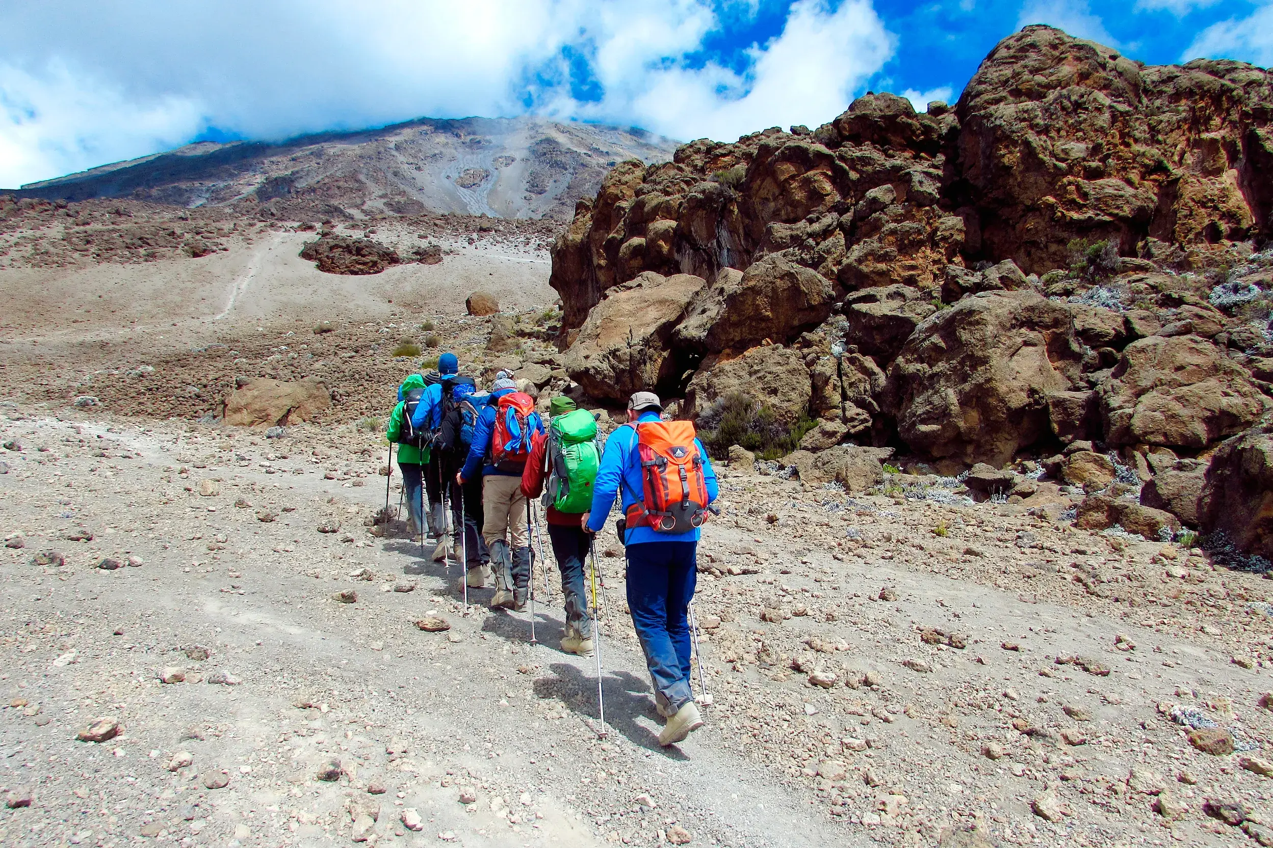 Eine Trekkinggruppe mit Rucksäcken wandert über den steinigen Kibo-Sattel auf dem Weg zum Gipfel des Kilimanjaro.