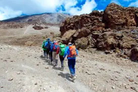 Eine Trekkinggruppe mit Rucksäcken wandert über den steinigen Kibo-Sattel auf dem Weg zum Gipfel des Kilimanjaro.