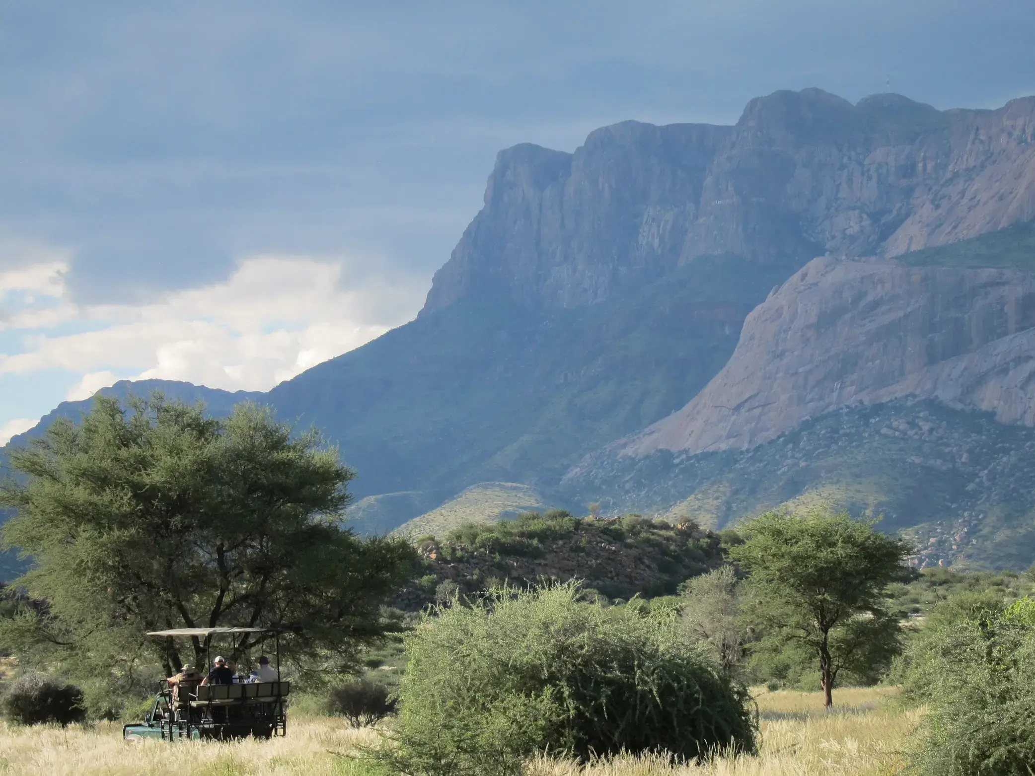 Reisegruppe auf Gamedrive im offenen Geländewagen durch die Savanne vor der markanten Bergkulisse des Erongo-Gebirges.