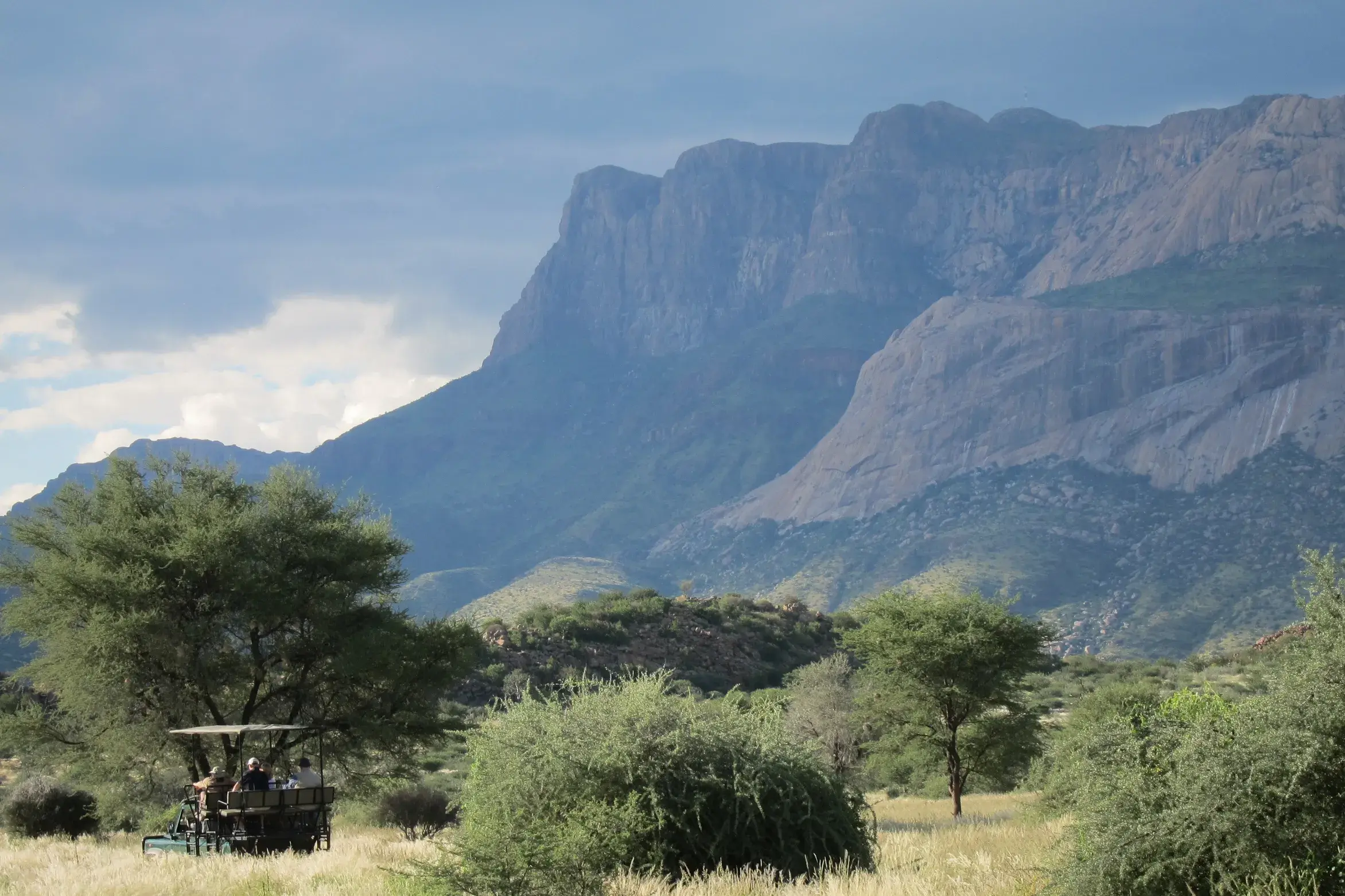 Reisegruppe auf Gamedrive im offenen Geländewagen durch die Savanne vor der markanten Bergkulisse des Erongo-Gebirges.
