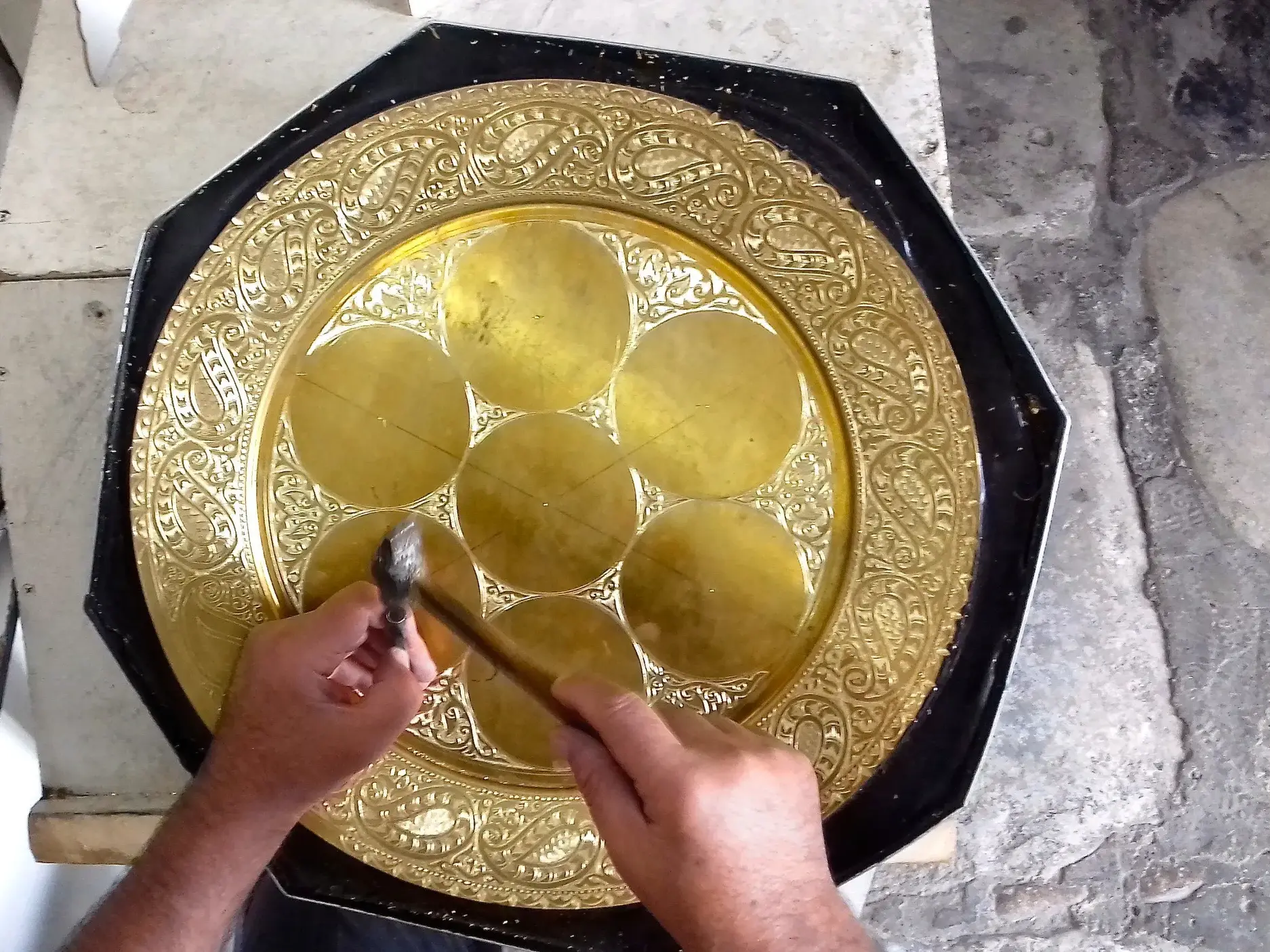 Ein usbekischer Ziseleur ziseliert mit Hammer und Meißel filigrane, orientalische Muster in eine achteckige Goldplatte.