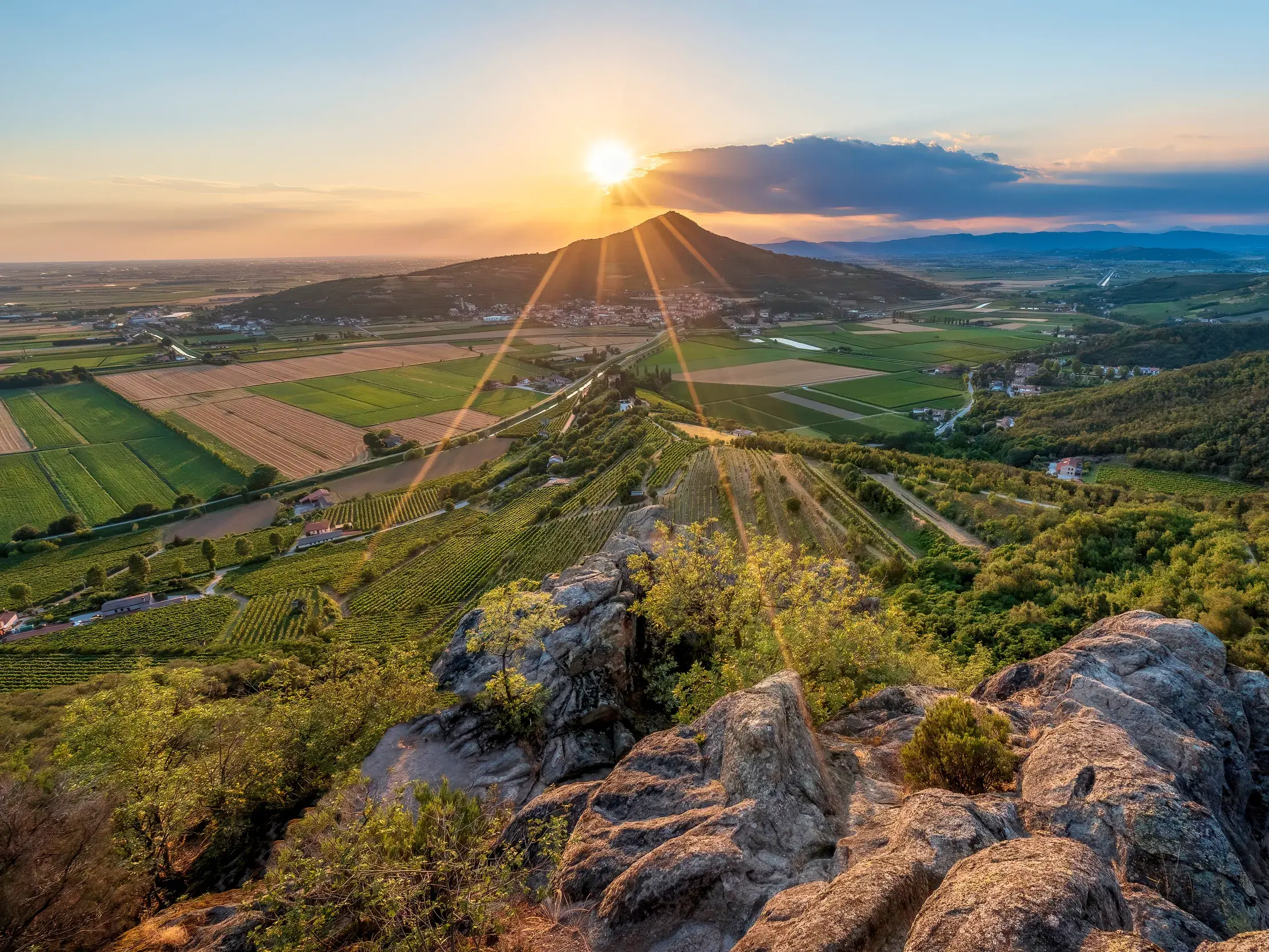 Idyllischer Blick von einem Felsen über Weinberge und Felder in den Euganeischen Hügeln bei Sonnenuntergang.