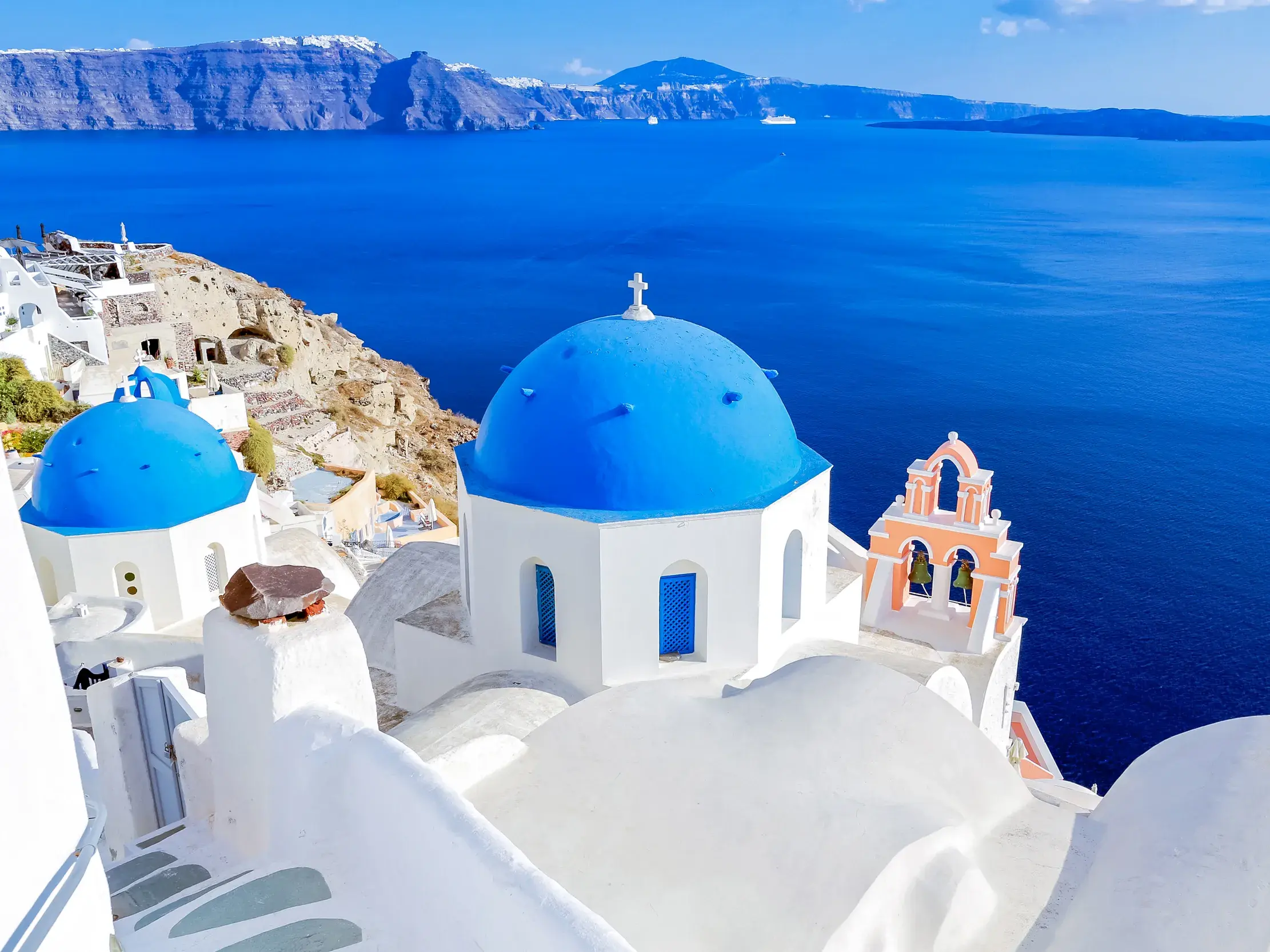 Markante weiße Kirchen mit blauen Kuppeln im Ort Ia auf der Kykladen-Insel Santorin, mit weitem Blick auf die Caldera.