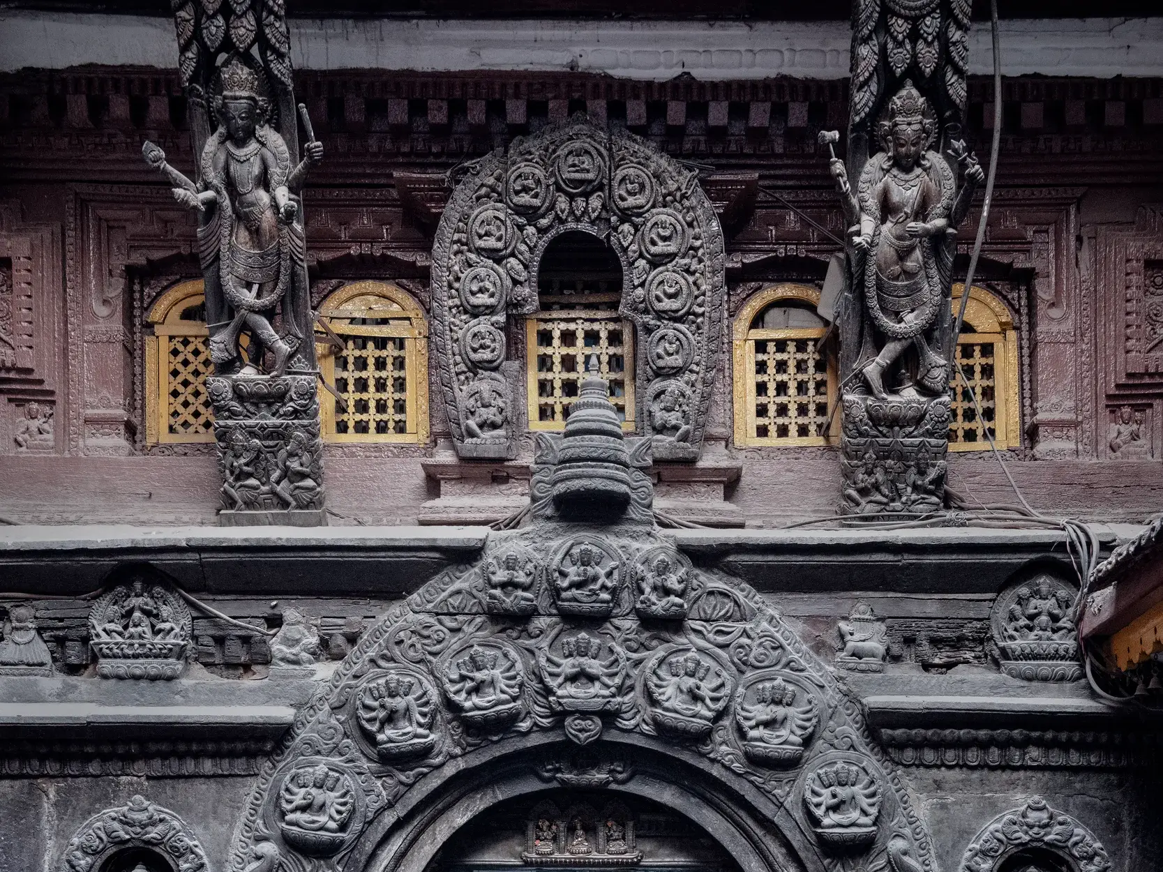Kunstvolle, dunkle Holzschnitzereien am Palast von Patan, einer Königsstadt in Nepal, mit Götterfiguren und Goldfenstern.