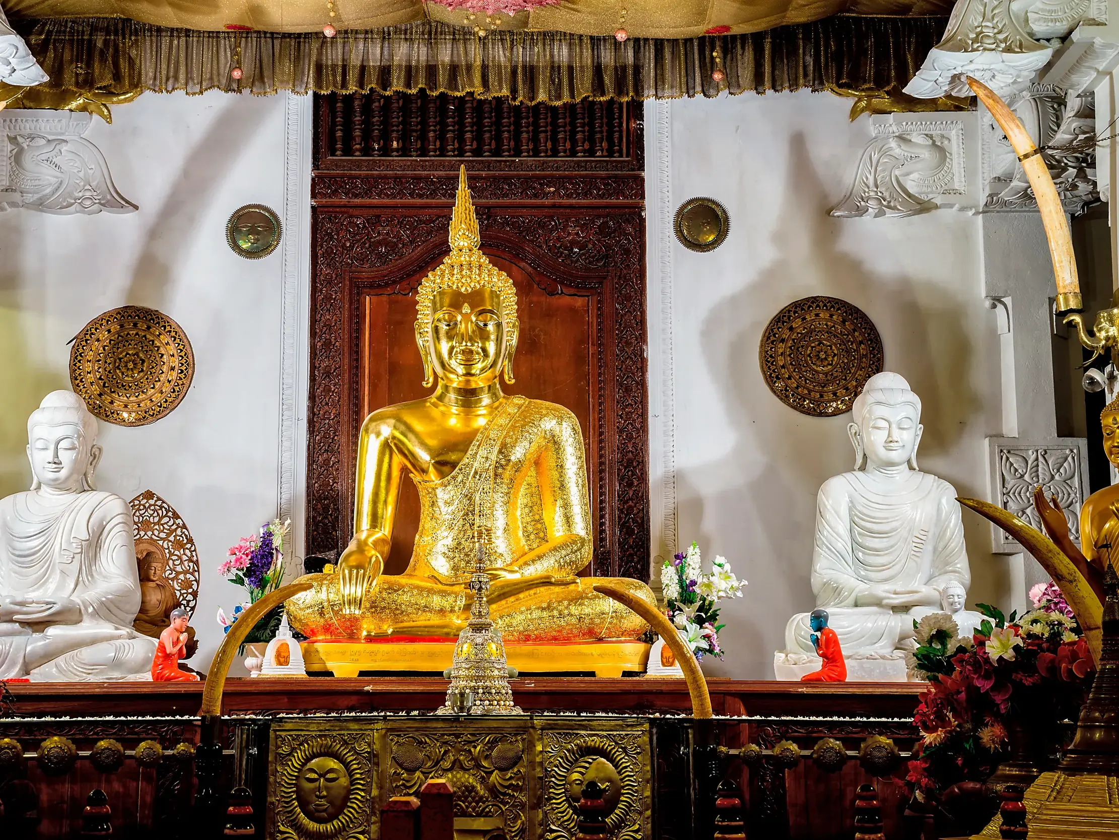 Prunkvoller Altar mit goldener Buddha-Statue, flankiert von weißen Figuren und Stoßzähnen im Zahntempel von Kandy.