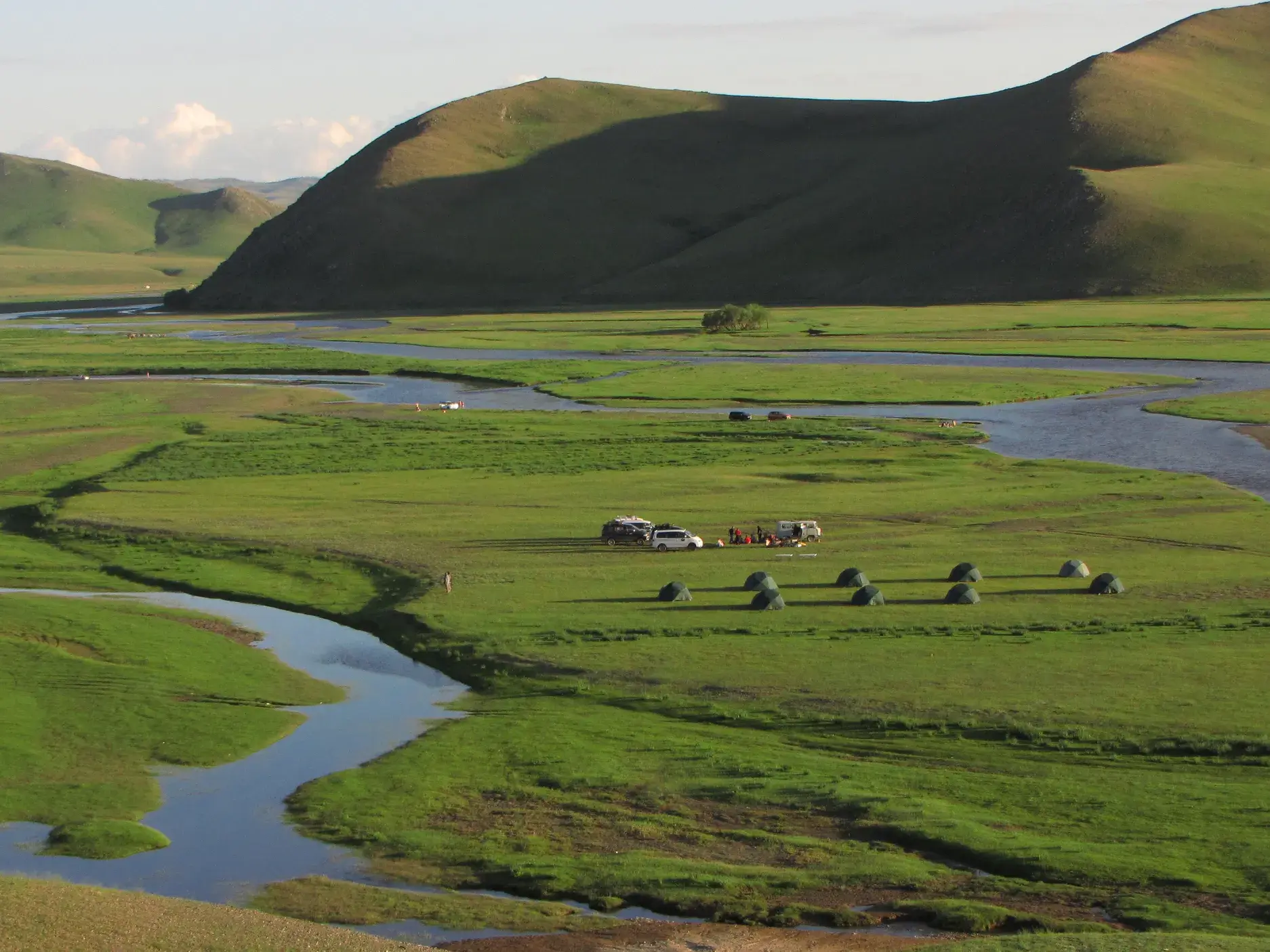 Zeltlager einer Trekking-Reisegruppe in einem weiten, grünen Tal am Flussufer im Khan-Khentii-Nationalpark in der Mongolei.