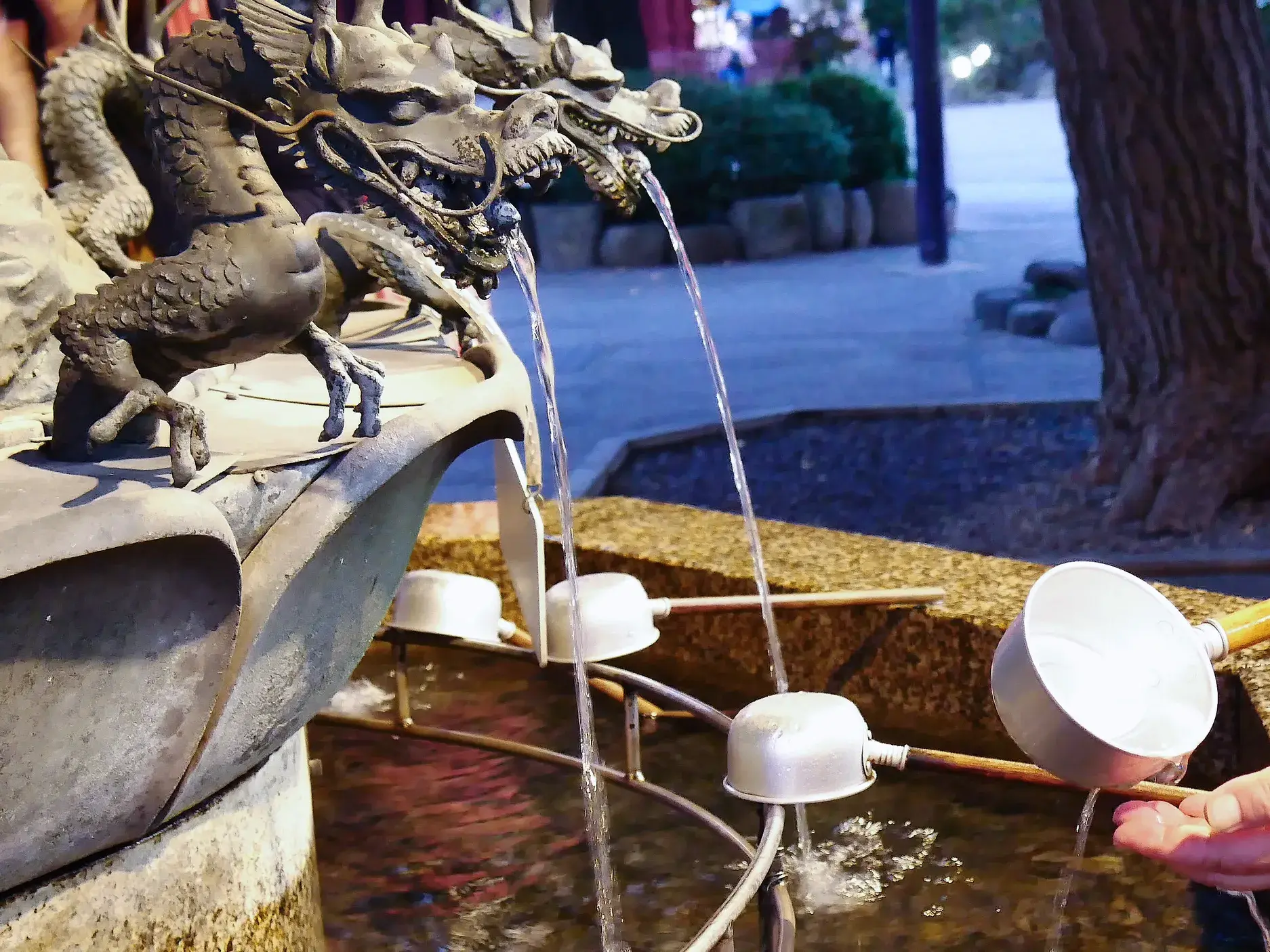 Eine Person bei der rituellen Handreinigung an einem Drachenbrunnen des Ikuta-Schreins in Kobe, Japan.