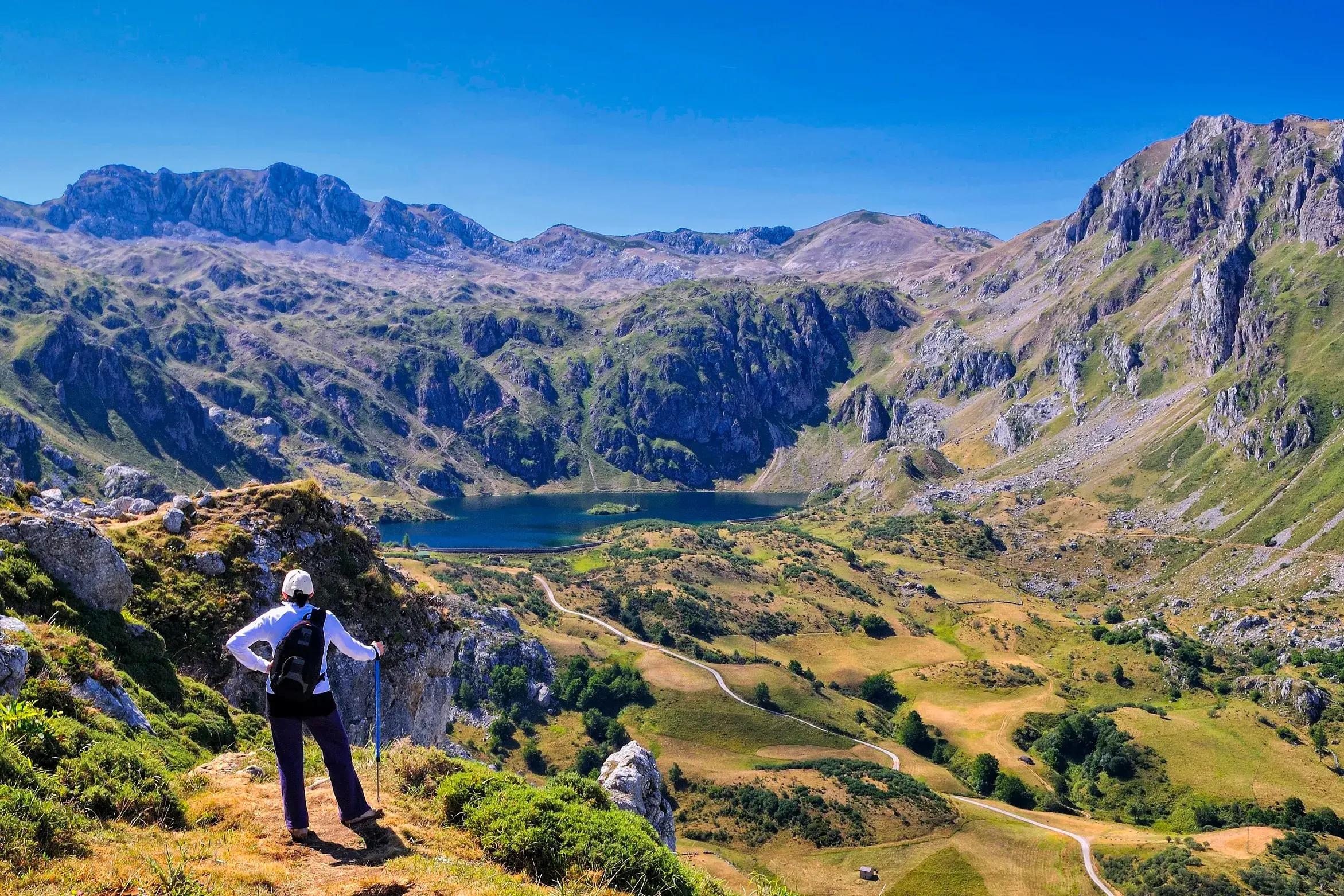 Eine Wanderin mit Rucksack und Stöcken genießt den Panoramablick auf die Saliencia-Seen im Naturpark Somiedo in Asturien.