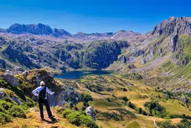 Eine Wanderin mit Rucksack und Stöcken genießt den Panoramablick auf die Saliencia-Seen im Naturpark Somiedo in Asturien.