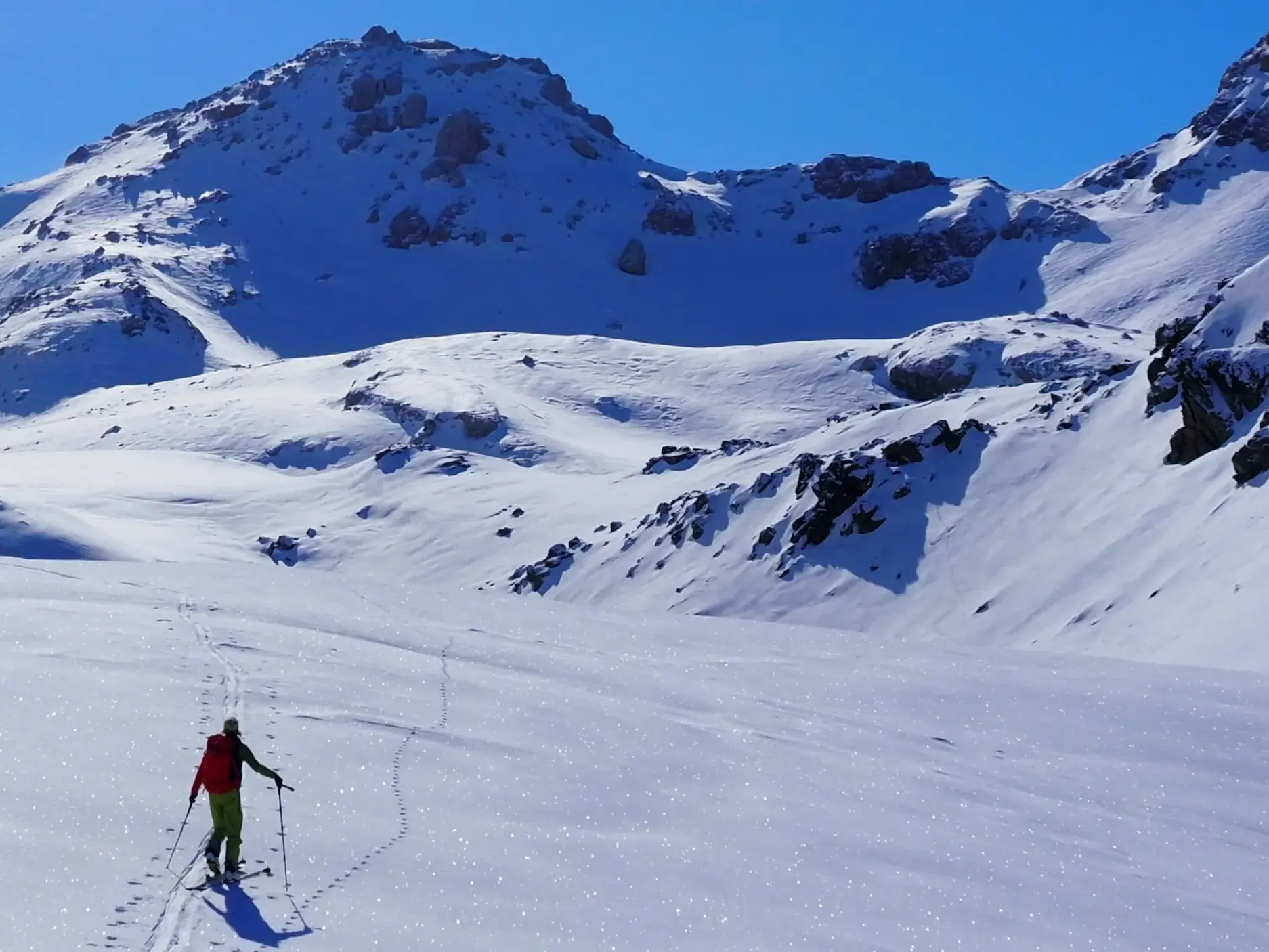 Ein Skitourengeher steigt bei strahlendem Sonnenschein durch ein weites Schneetal zum Gipfel des Korab in Albanien auf.