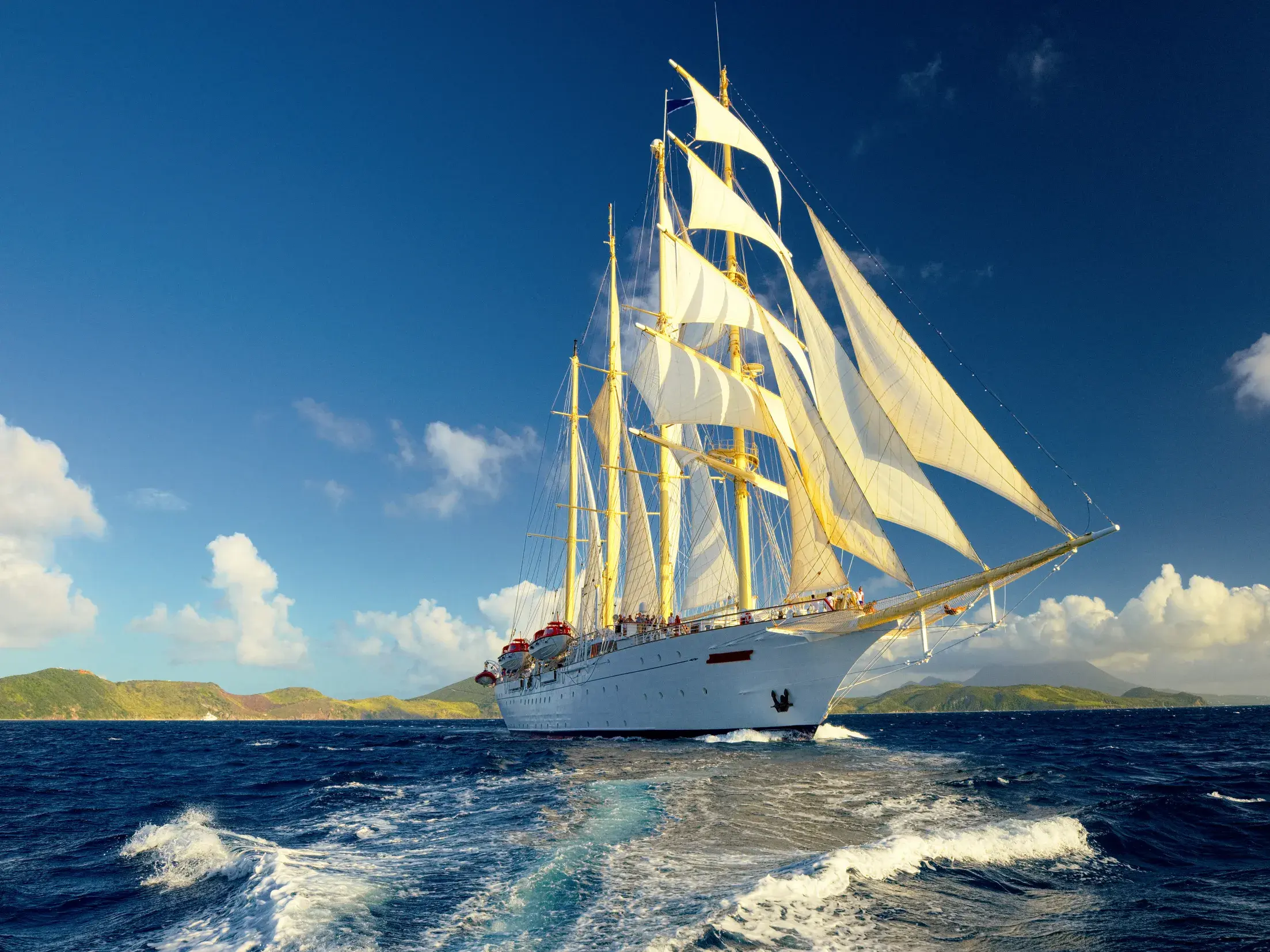 Der majestätische Großsegler Star Flyer mit weißen Segeln kreuzt auf dem blauen Meer entlang der Küste der Kleinen Antillen.