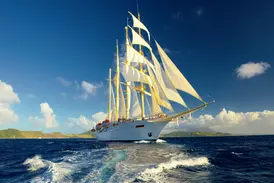 Der majestätische Großsegler Star Flyer mit weißen Segeln kreuzt auf dem blauen Meer entlang der Küste der Kleinen Antillen.