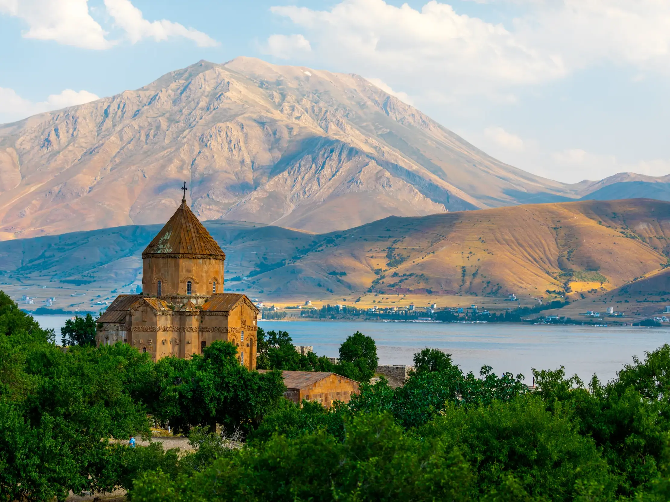 Die armenische Heiligkreuzkirche auf der Insel Akdamar im Van-See vor einer imposanten Bergkulisse in der Osttürkei.