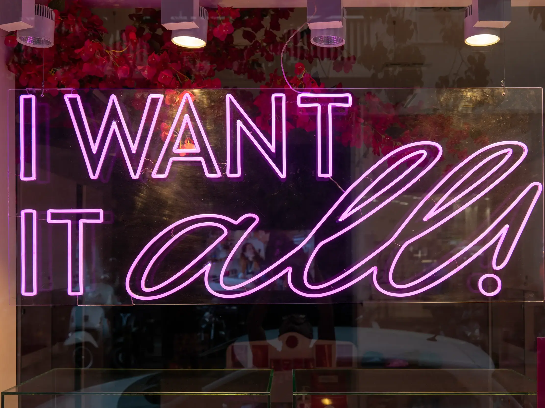 Pink leuchtende Neonschrift 'I want it all' in einem Schaufenster, Symbol für den urbanen Lifestyle in den Szenevierteln Athens.