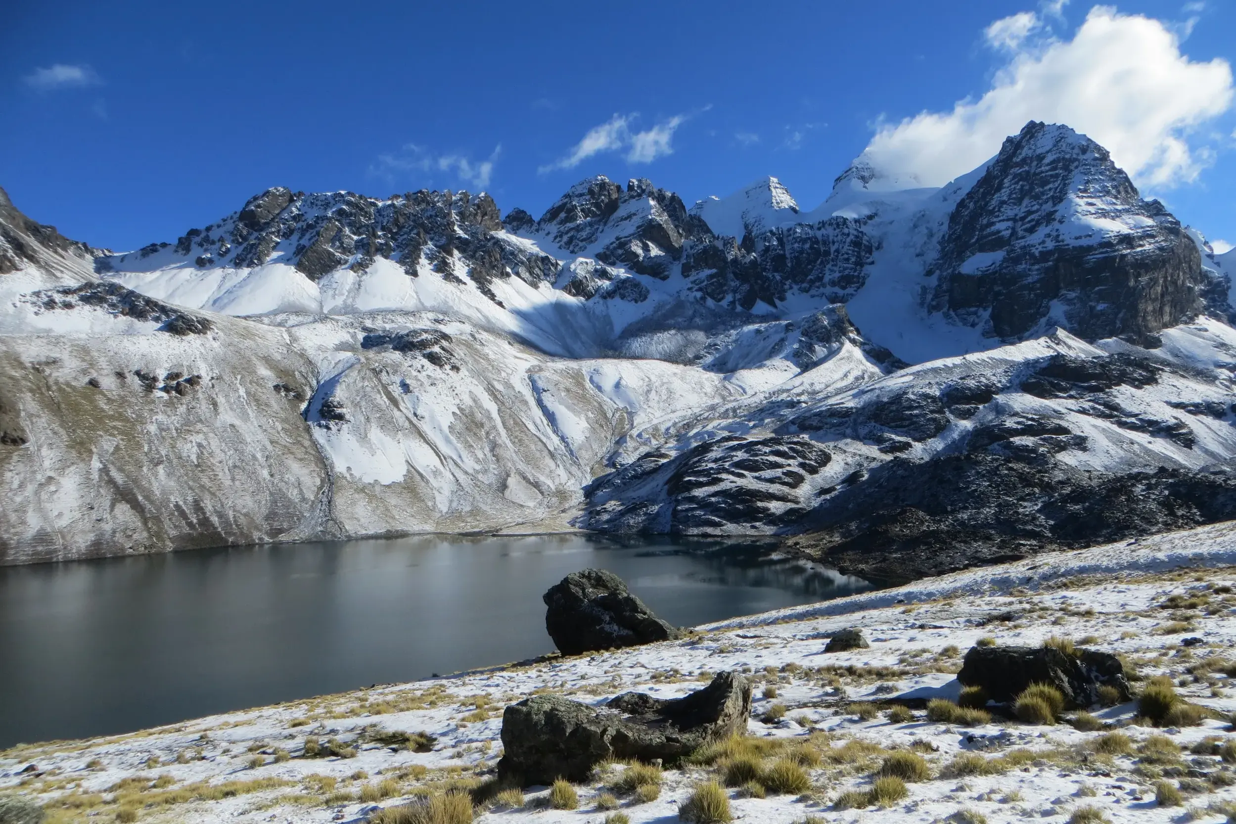 Imposante, schneebedeckte Gipfel der Königskordillere in Bolivien ragen über der dunklen Laguna Chiar Khota auf.