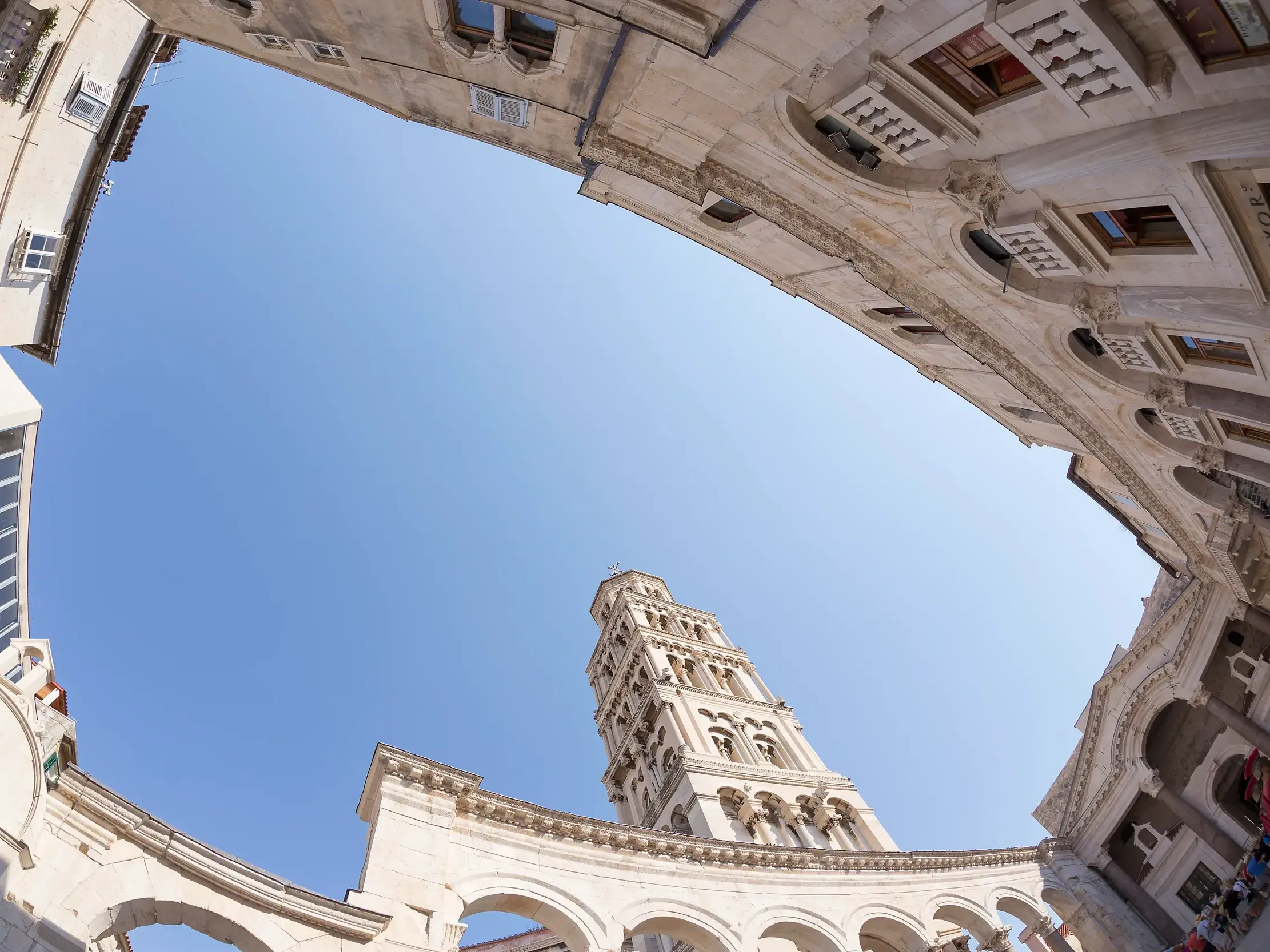 Weitwinkel-Blick aus dem Innenhof des Diokletian-Palastes in Split nach oben zum historischen Glockenturm und blauen Himmel.
