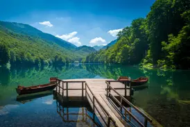 Ein Holzsteg mit Ruderbooten am spiegelglatten Biogradsko See, umgeben von den dichten Wäldern des Nationalparks in Montenegro.