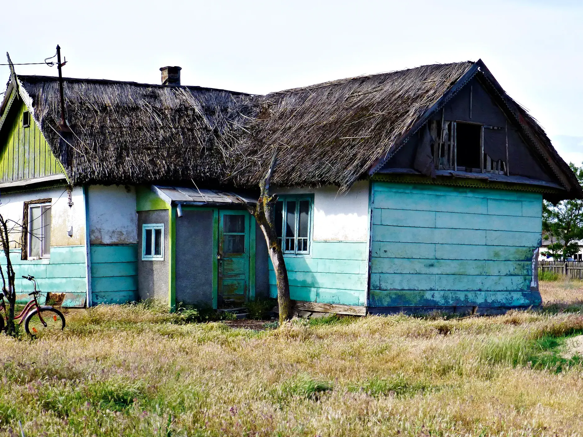 Rustikales Haus mit verwittertem Schilfdach und türkiser Fassade, davor ein Fahrrad in einer Wiese im Donaudelta.