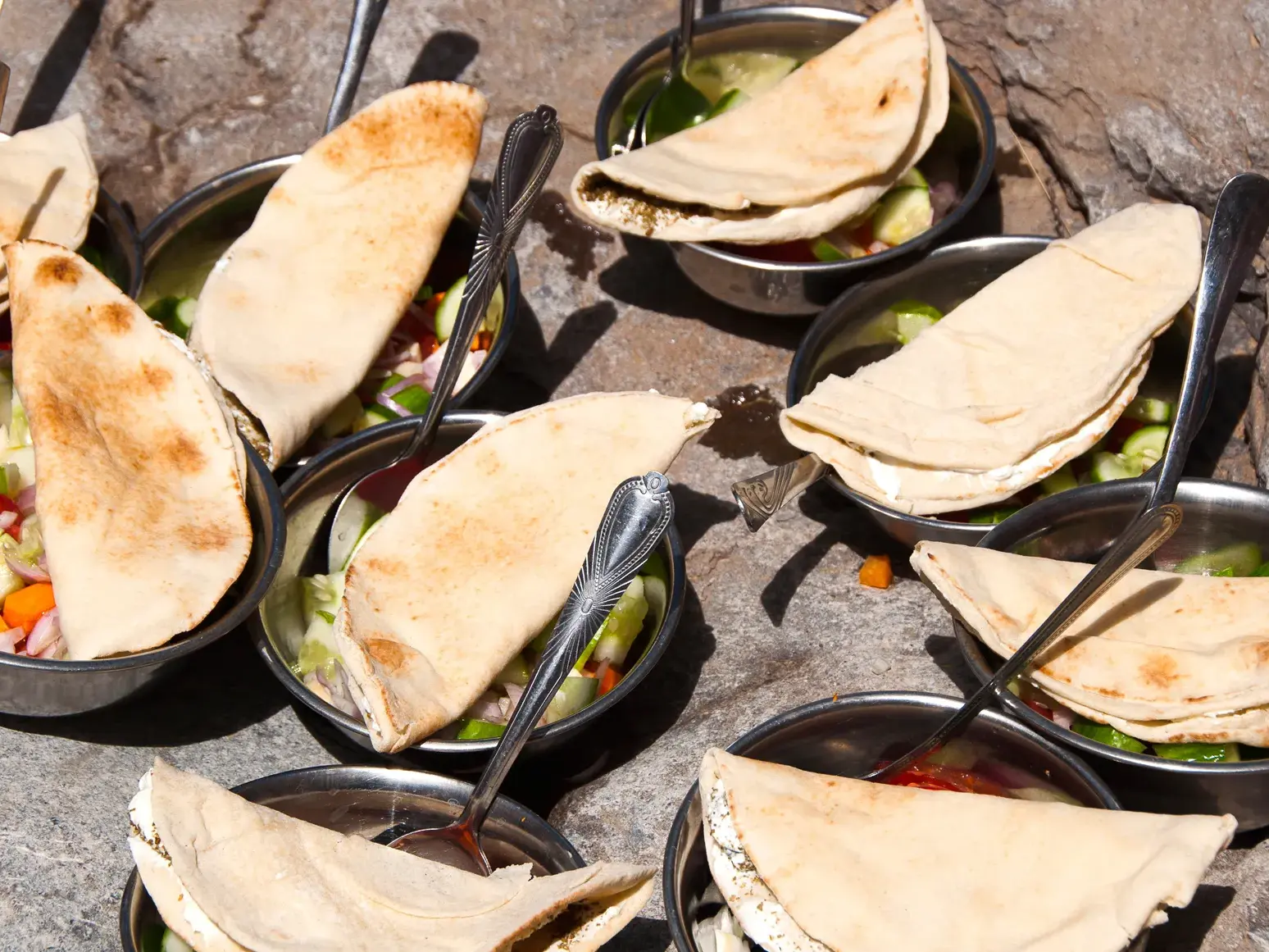 Frisches Mittagessen beim Trekking im Oman: Metallschalen mit Salat und arabischem Fladenbrot auf felsigem Untergrund.