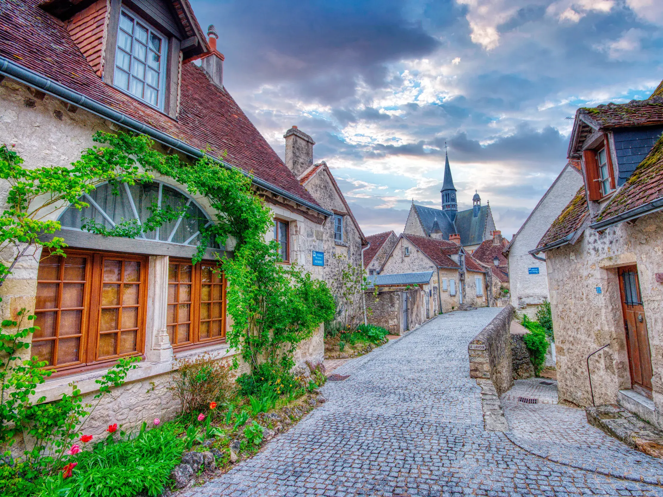 Eine kopfsteingepflasterte Gasse in der mittelalterlichen Altstadt von Loches mit alten Steinhäusern und einer Kirche im Hintergrund.