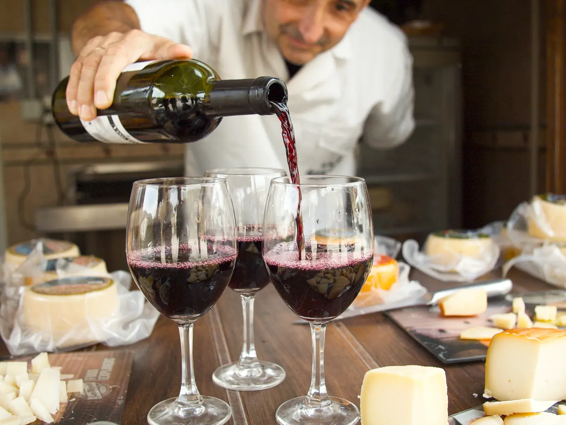 Bei einer Weinprobe in der spanischen Region La Rioja füllt ein Mann Gläser mit Rotwein, umgeben von regionalen Käsespezialitäten.