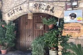 Der charmante Eingang des Restaurants Cueva Reina in Alquézar mit rustikalem Steinbogen, Holztür und üppigen Grünpflanzen.