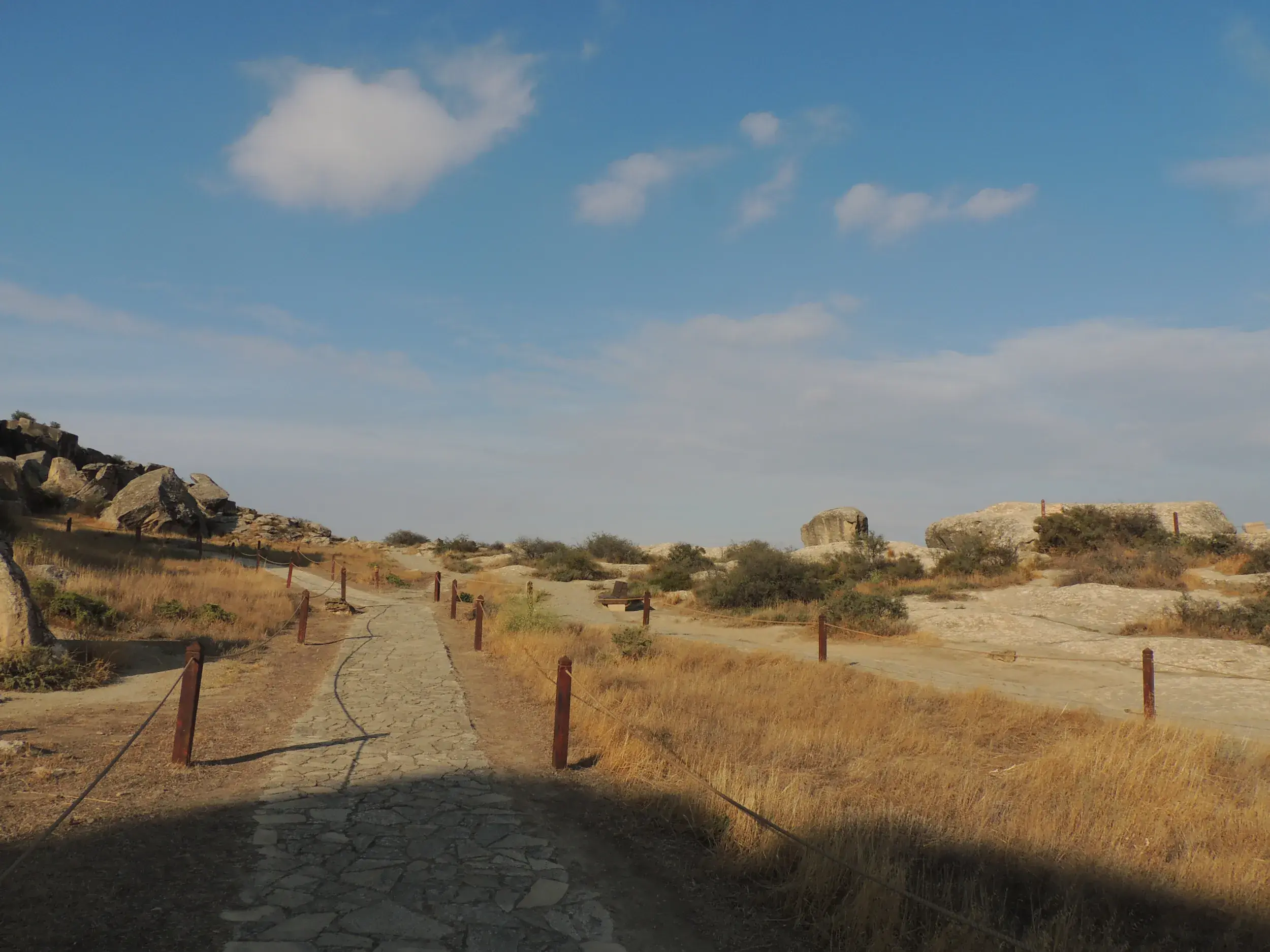 Ein steiniger Wanderweg führt durch die sonnige, karge Felslandschaft des Qobustan-Nationalparks in Aserbaidschan.