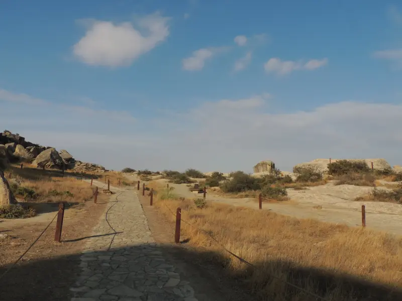Ein steiniger Wanderweg führt durch die sonnige, karge Felslandschaft des Qobustan-Nationalparks in Aserbaidschan.