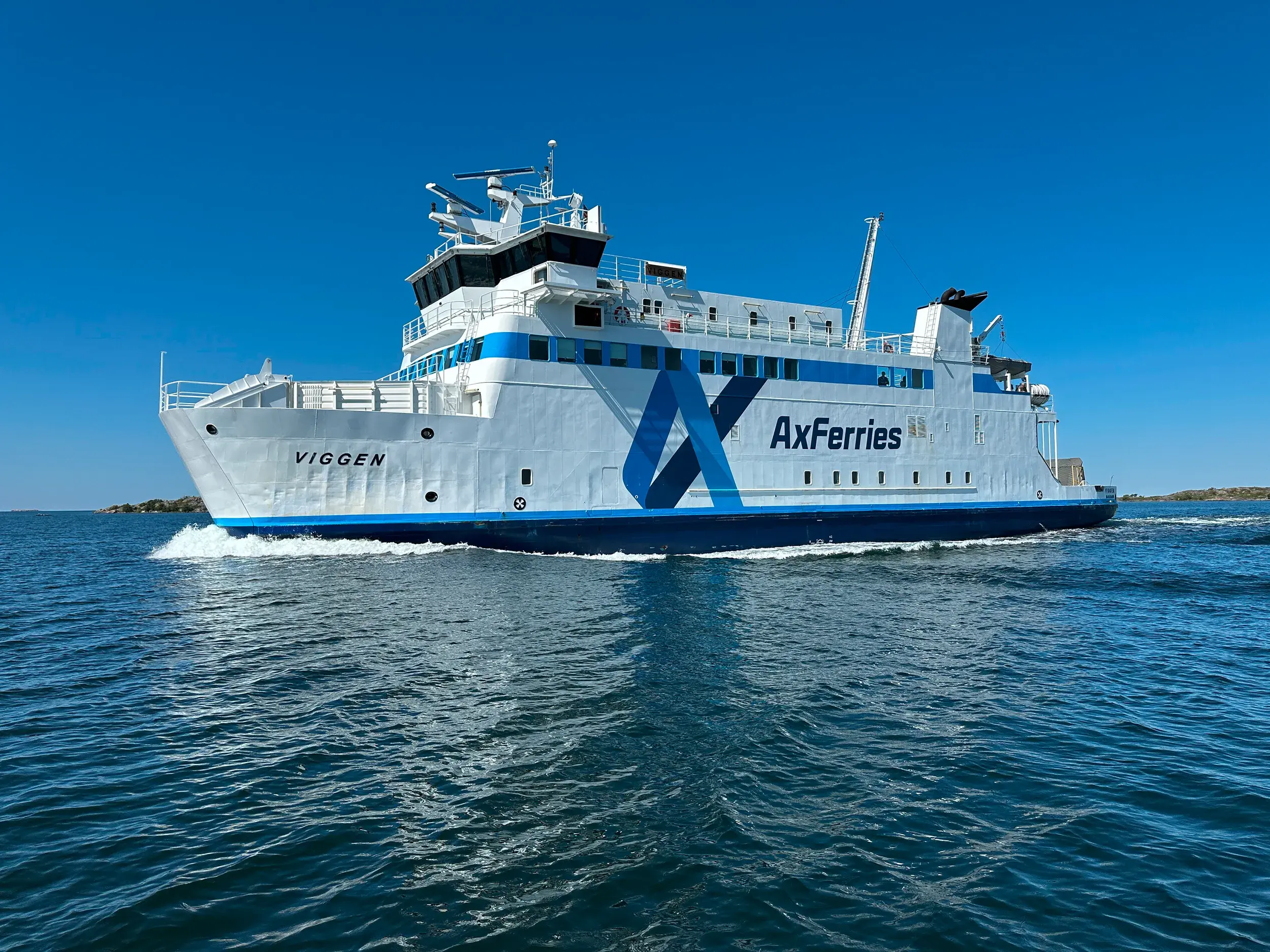 Die weiß-blaue Fähre Viggen von AxFerries fährt bei Sonnenschein durch den Schärengarten der finnischen Alandinseln.