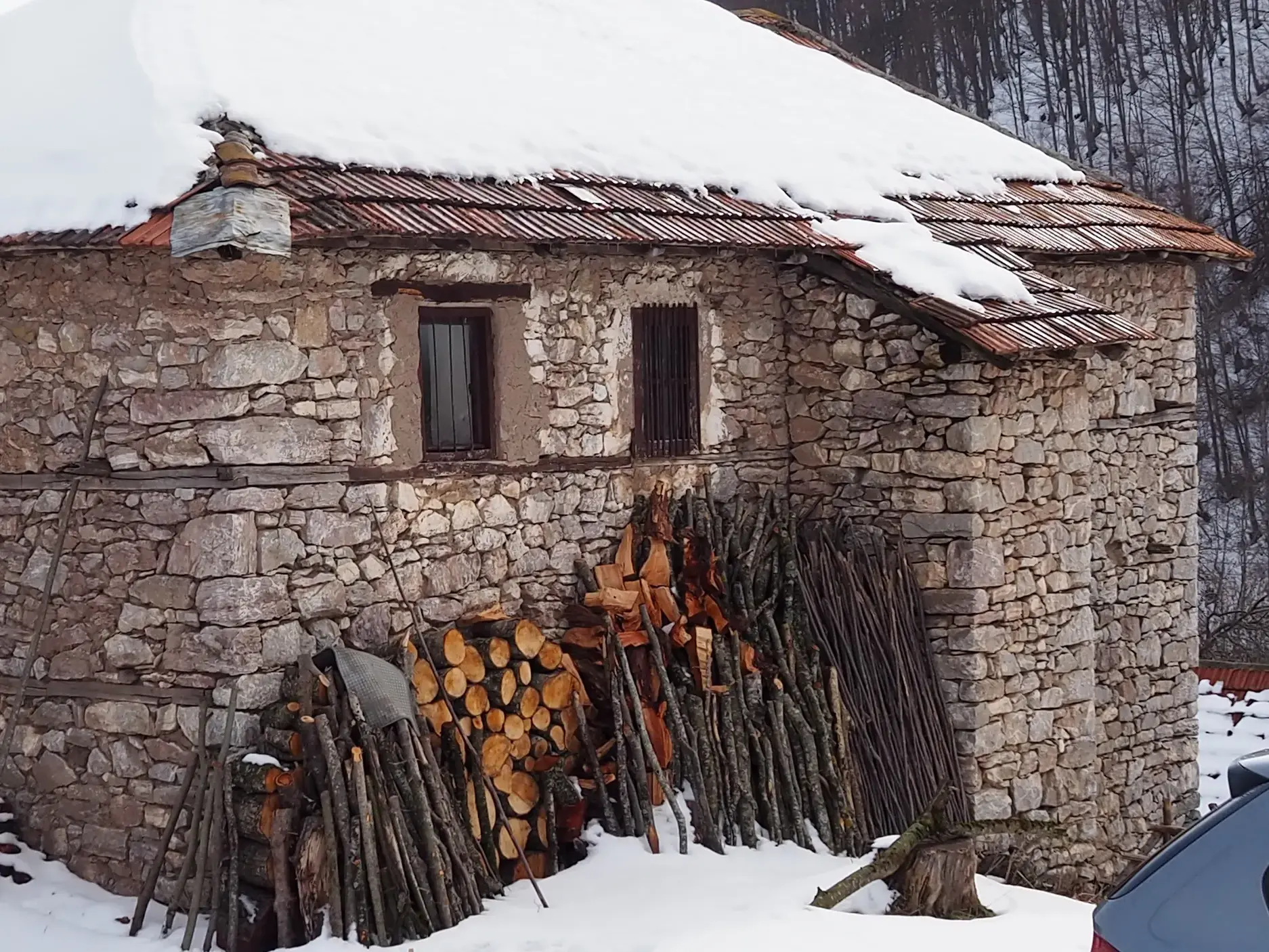 Landestypisches Steinhaus in den Bergen des Balkans mit schneebedecktem Dach und gestapeltem Brennholz an der Fassade.