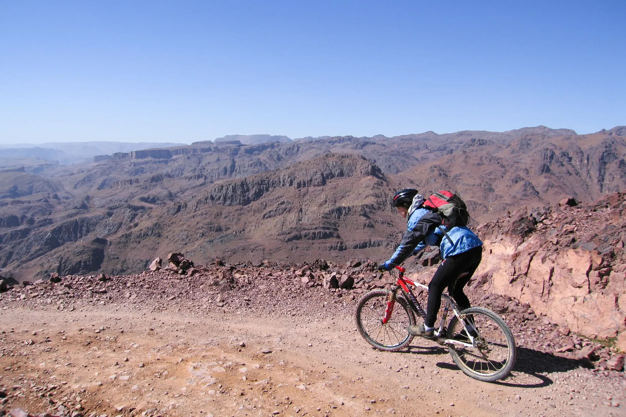 Ein Mountainbiker fährt auf einer steinigen Schotterpiste durch die weite, karge Felslandschaft des Jebel Sarhro in Marokko.