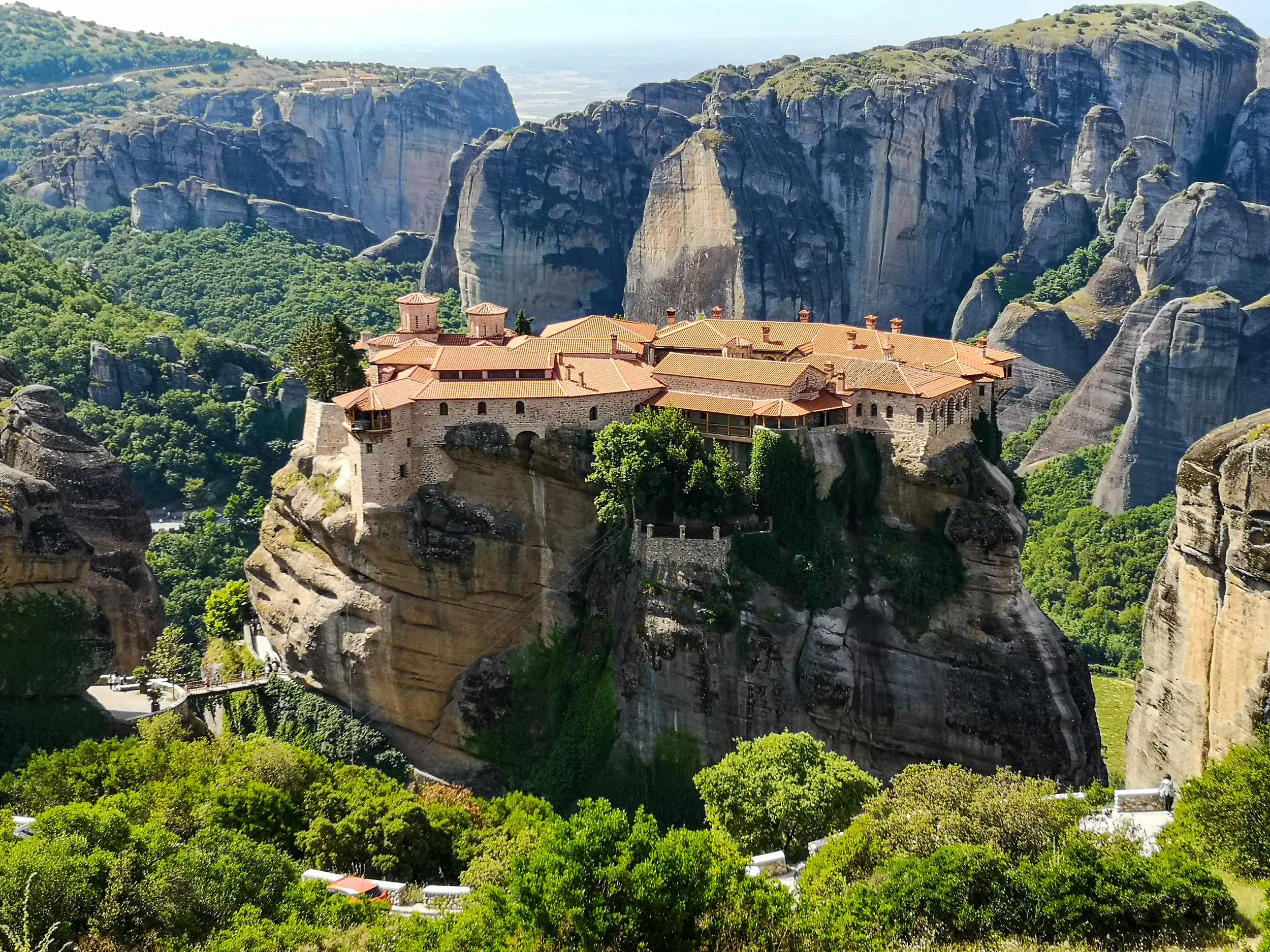 Ein Meteora Kloster thront auf einem riesigen Felsen, umgeben von der beeindruckenden, grünen Felslandschaft Griechenlands.