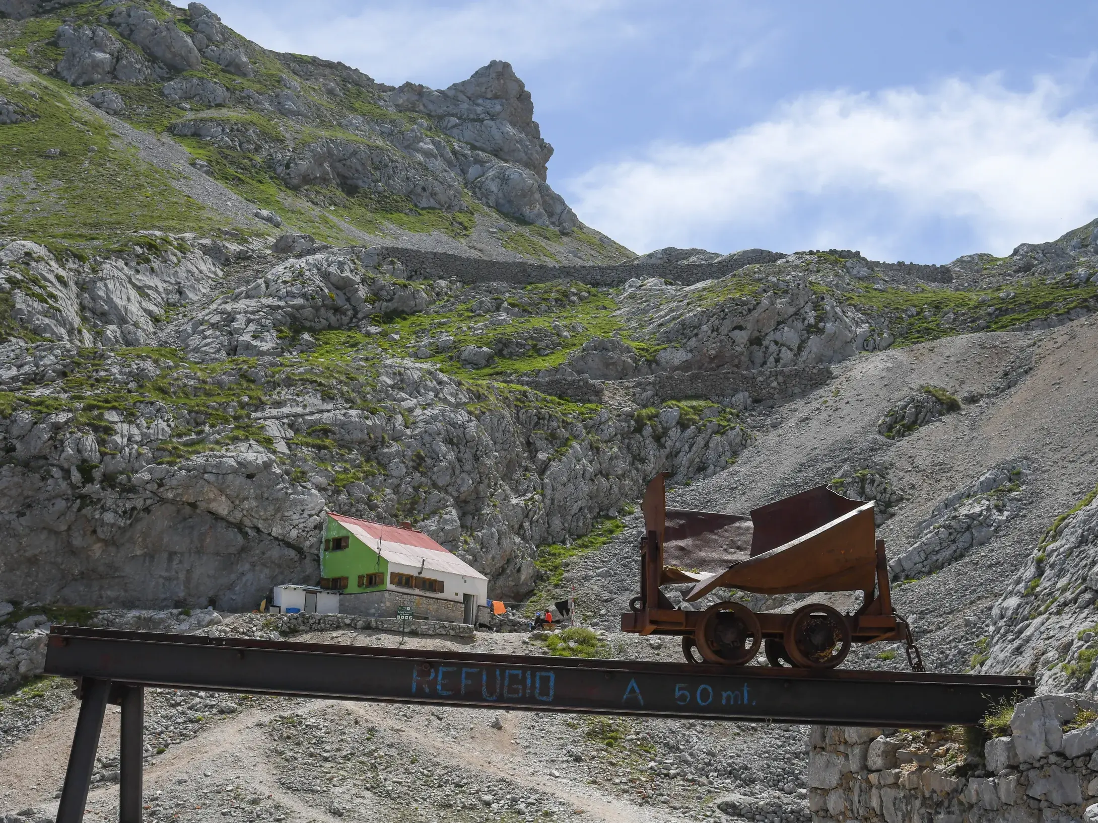 Eine alte, rostige Lore auf einem Stahlträger vor der in den Fels gebauten Schutzhütte Casetón de Ándara in Asturien.