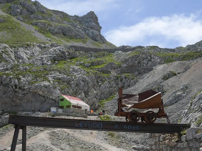 Eine alte, rostige Lore auf einem Stahlträger vor der in den Fels gebauten Schutzhütte Casetón de Ándara in Asturien.