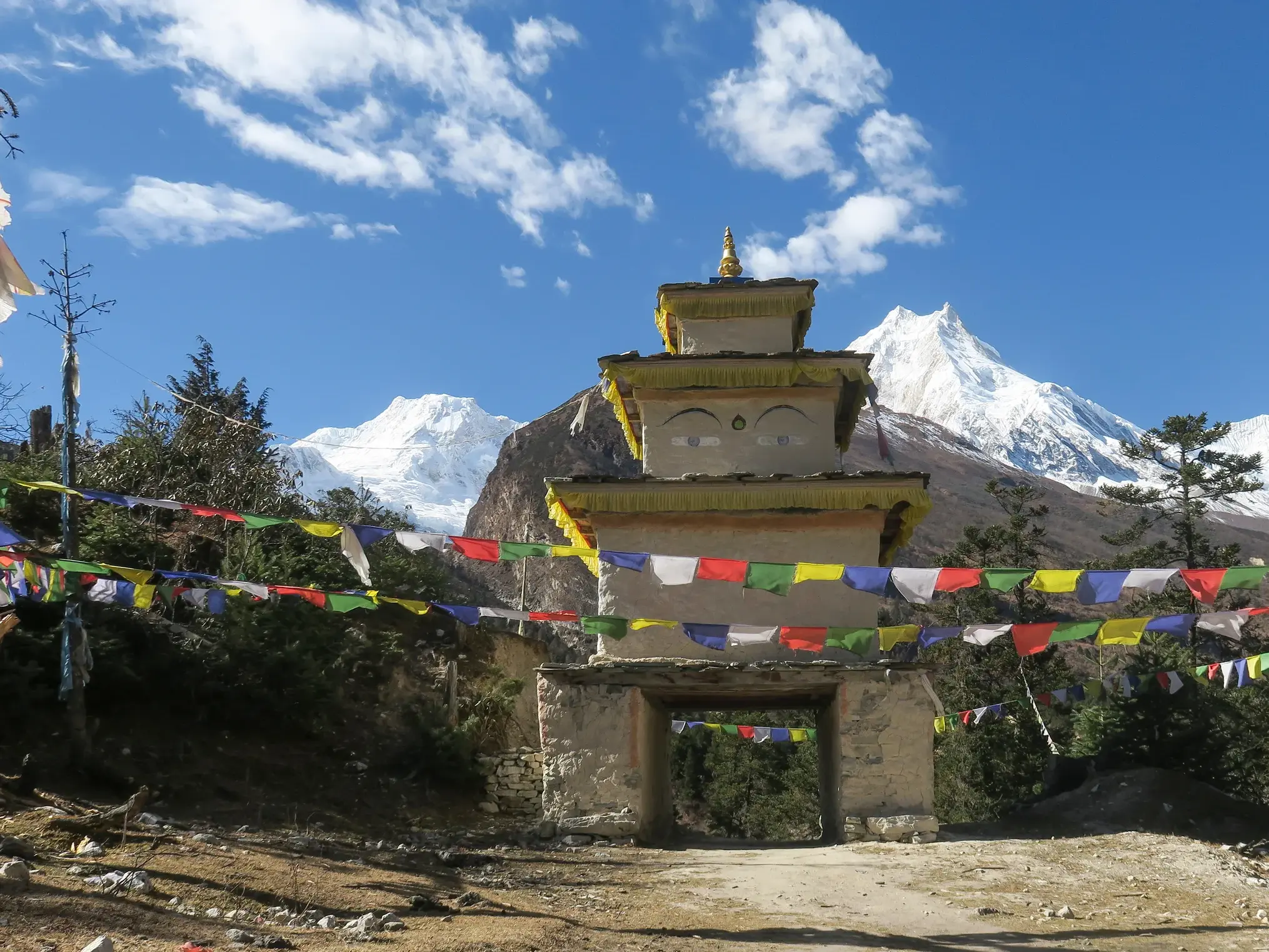 Ein traditioneller Tschörten, geschmückt mit bunten Gebetsfahnen, markiert den Trekkingpfad der Manaslu-Umrundung in Nepal.