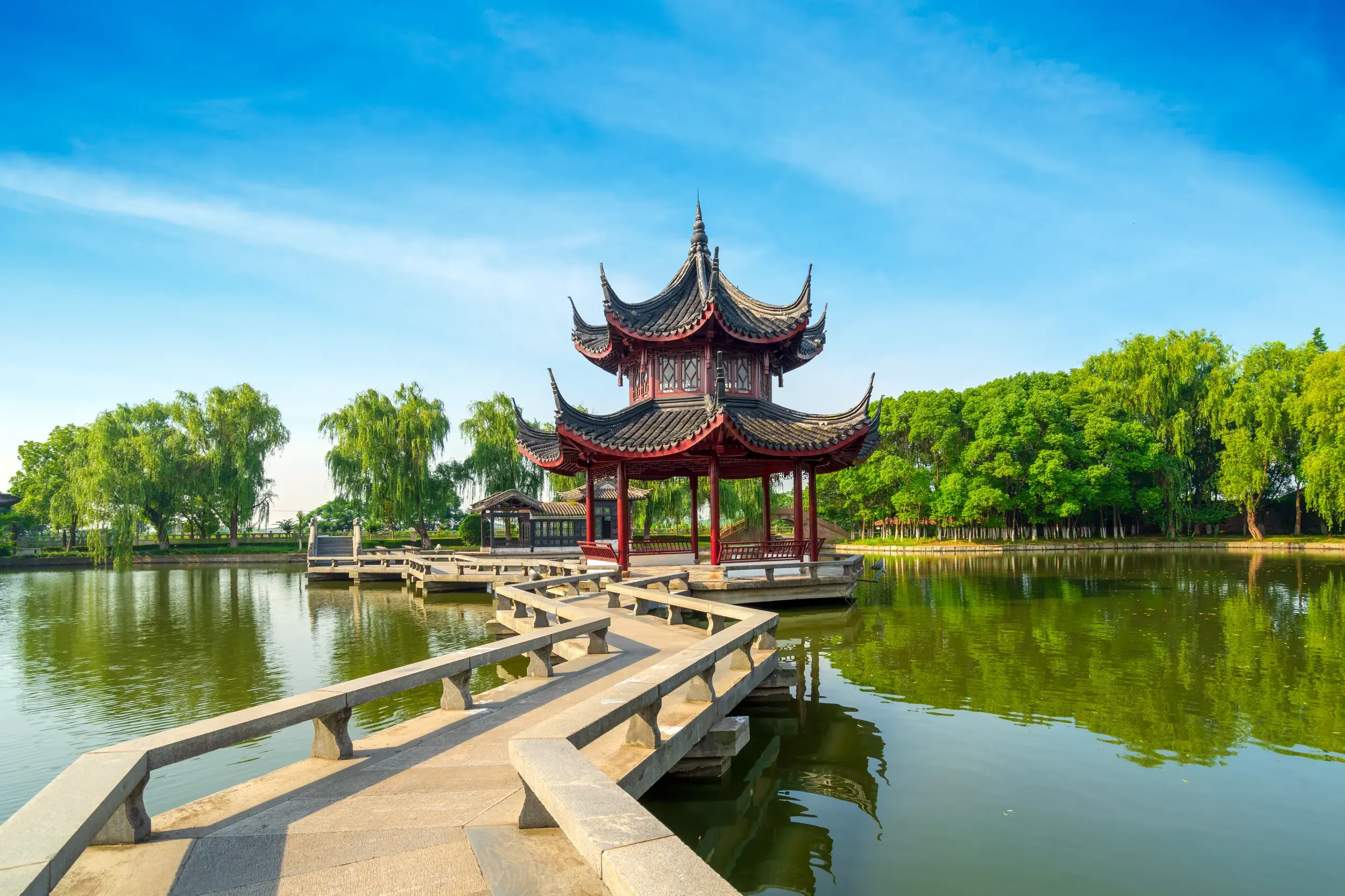Eine Steinbrücke führt zu einem traditionellen Pavillon auf einem See im kunstvollen Garten des Meisters der Netze in Suzhou.