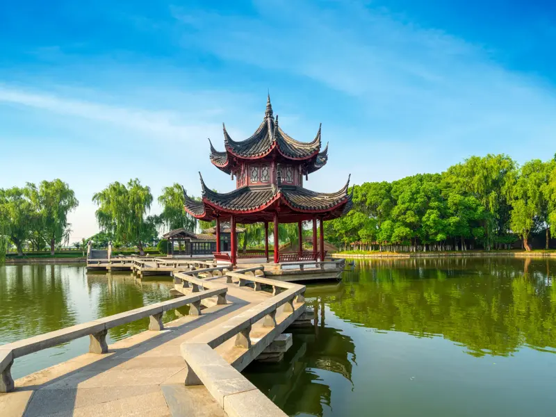 Eine Steinbrücke führt zu einem traditionellen Pavillon auf einem See im kunstvollen Garten des Meisters der Netze in Suzhou.