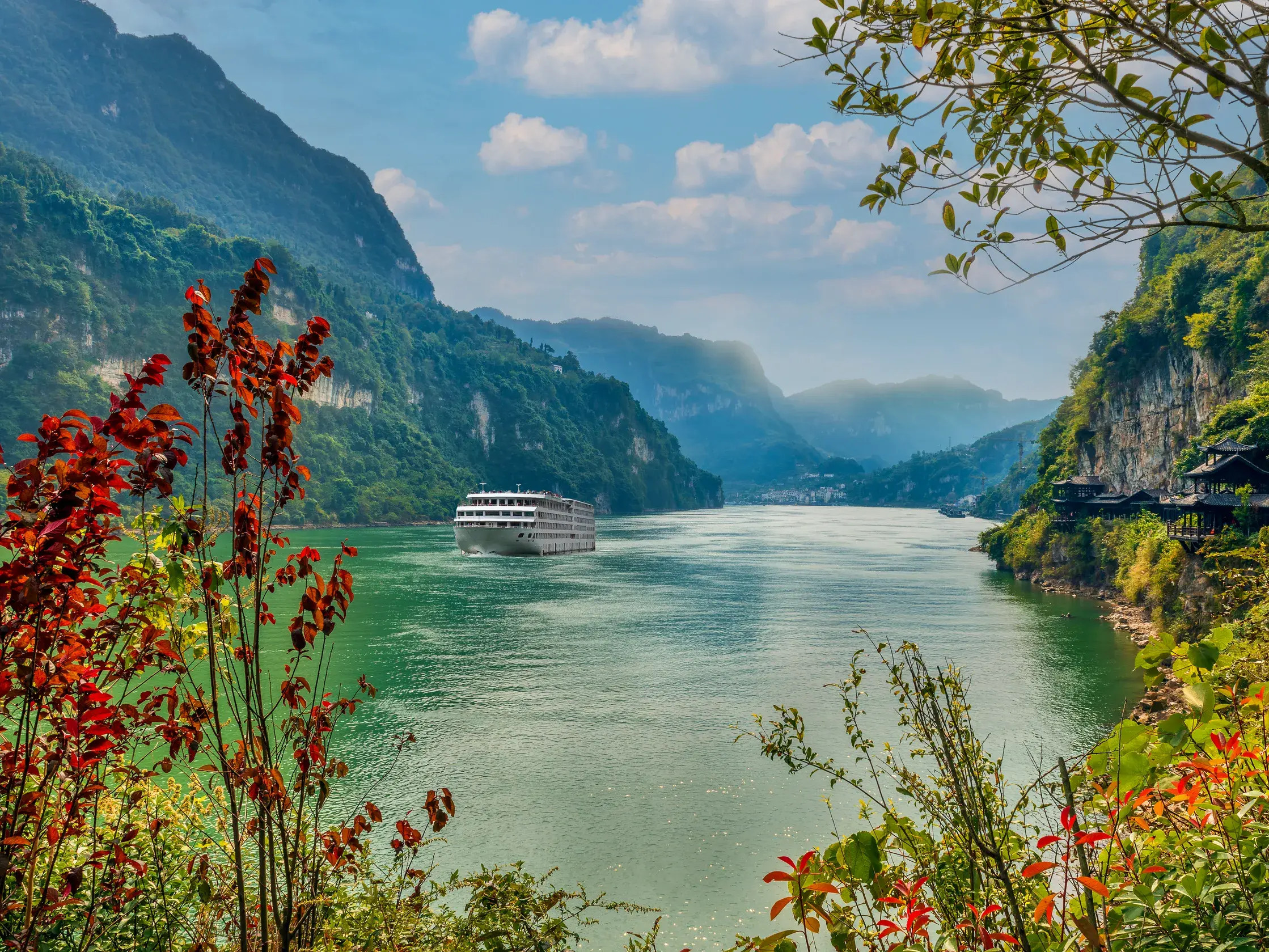 Ein weißes Flusskreuzfahrtschiff fährt auf dem Yangzi durch die beeindruckende, grüne Schluchtenlandschaft Chinas.