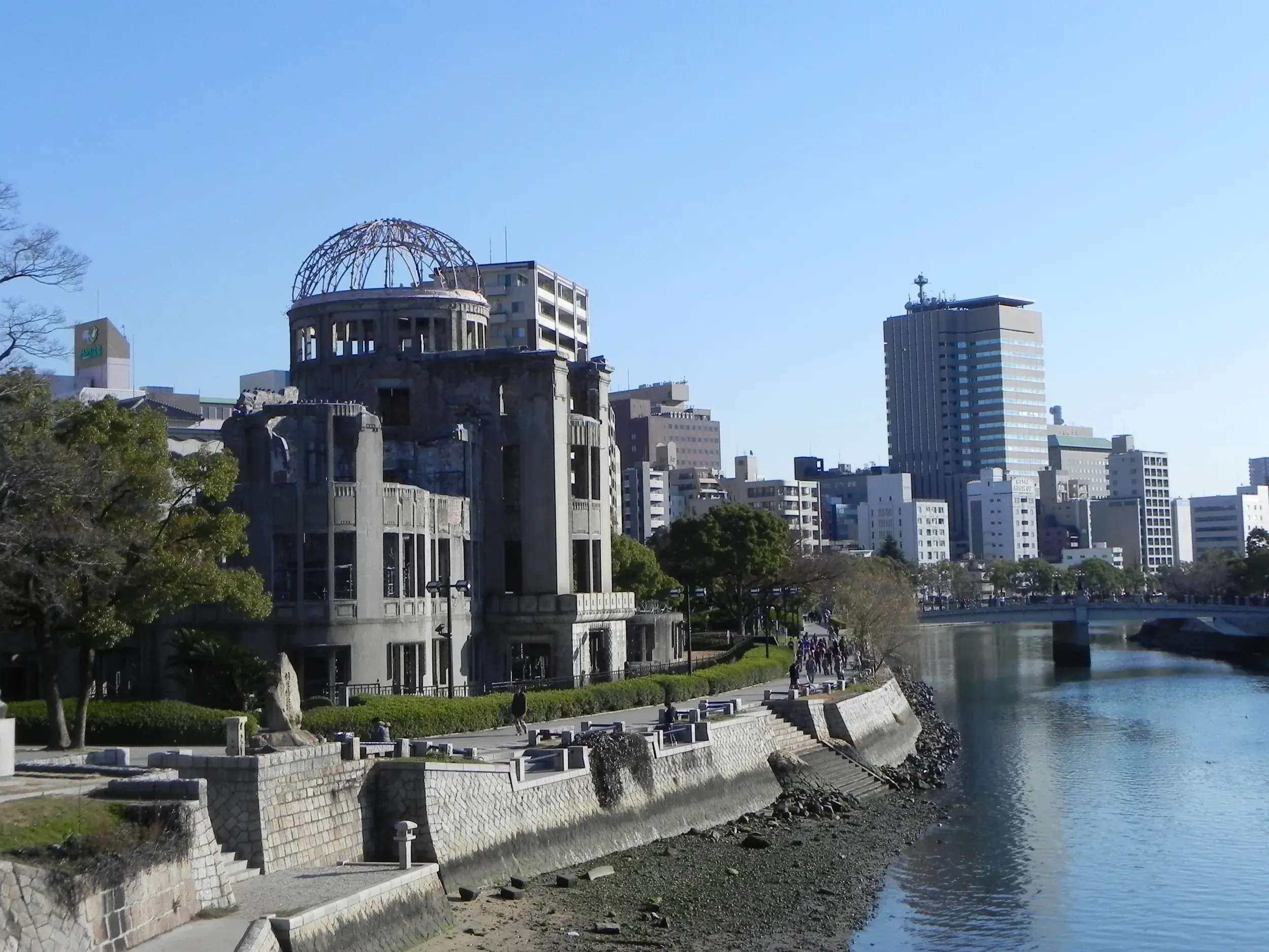 Der Atombombendom im Friedenspark Hiroshima steht als Mahnmal am Flussufer vor der modernen Skyline der Stadt.