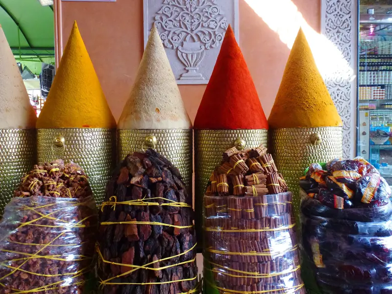 Bunte Gewürze wie Kurkuma und Zimtstangen, kunstvoll aufgetürmt in goldenen Gefäßen auf einem Souk in Marokko.